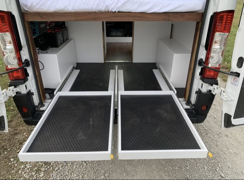 Efficient rv rental storage: Rear pull-out trays in a camper van conversion, with bed above and power system.. Ram Promaster 2020