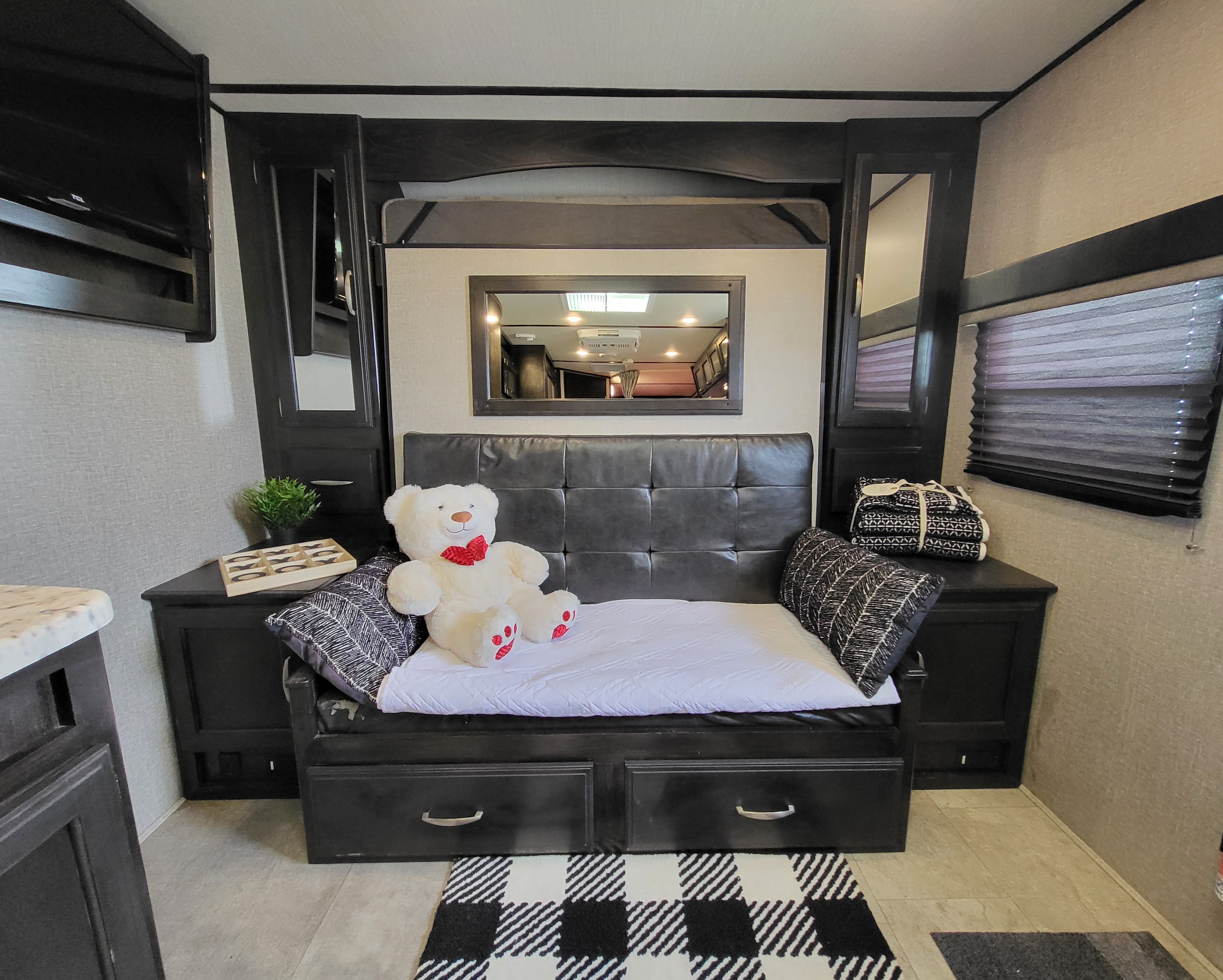 Cozy RV rental space featuring a black futon bed with storage, a teddy bear, and a tucked-away bunk. Modern design.. Grand Design Imagine XLS 2019