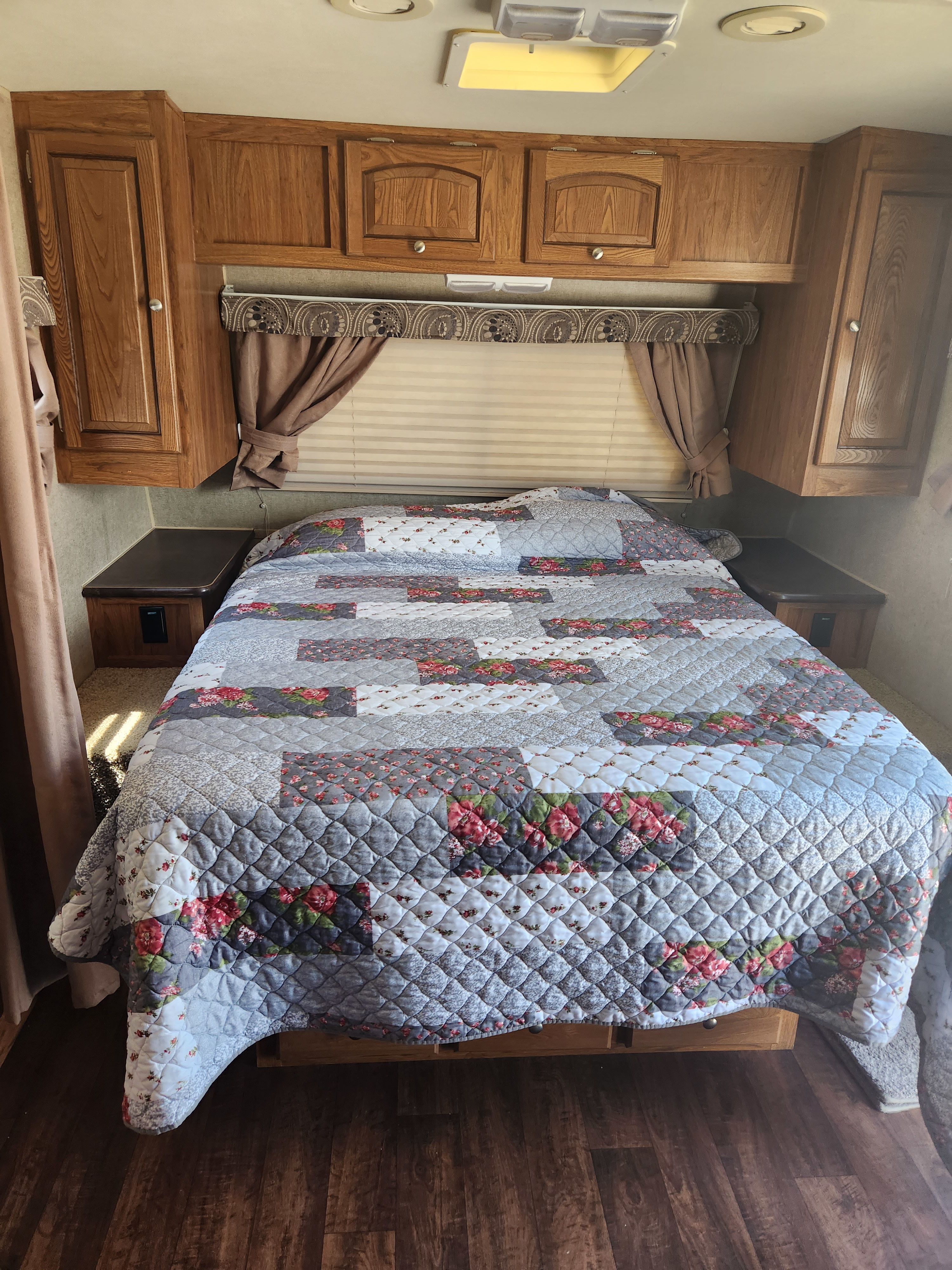 Cozy RV rental bedroom with a floral quilt, wood cabinets, and bedside tables, offering a comfortable space.. Forest River Rockwood Mini Lite 2013
