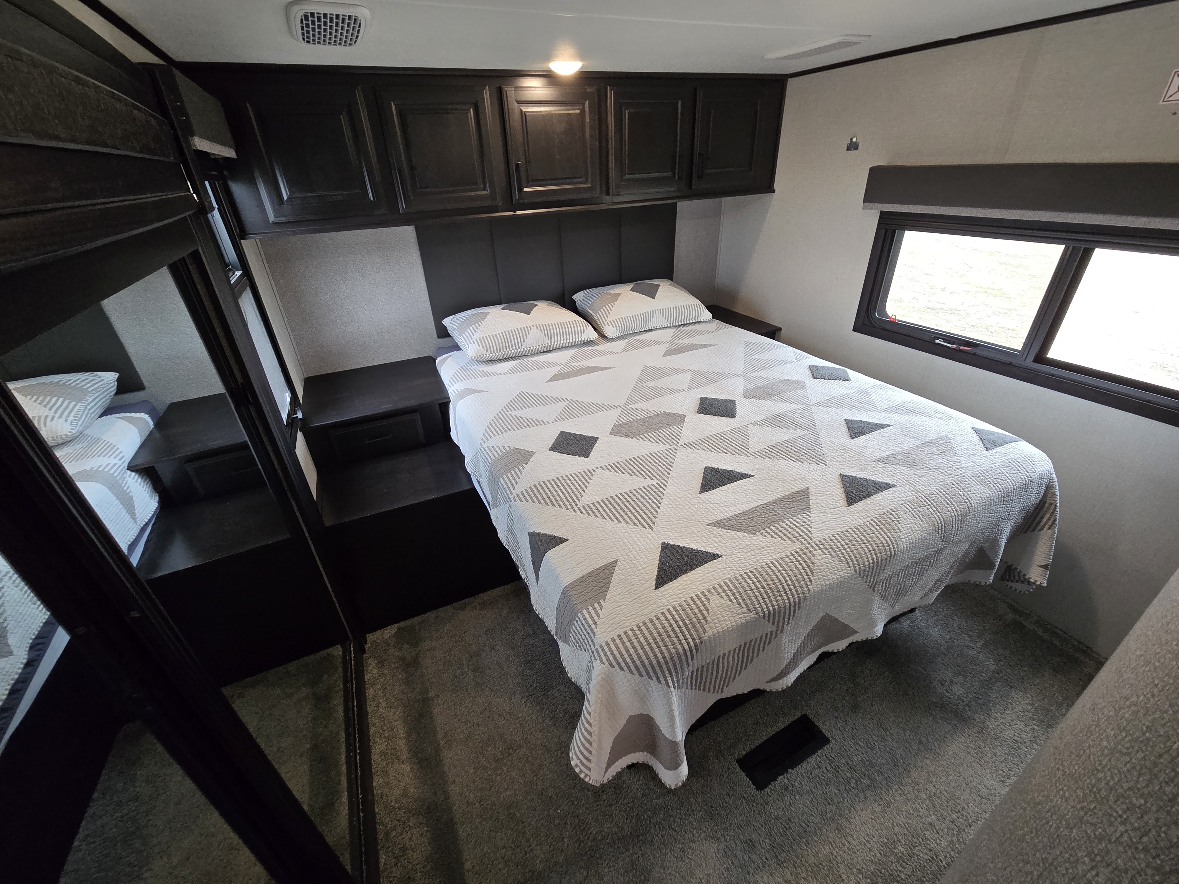 This cozy RV rental bedroom features a comfy bed with a geometric quilt, dark overhead cabinets, and side nightstands. Ready for adventure!. Open Range Highland Ridge 2021