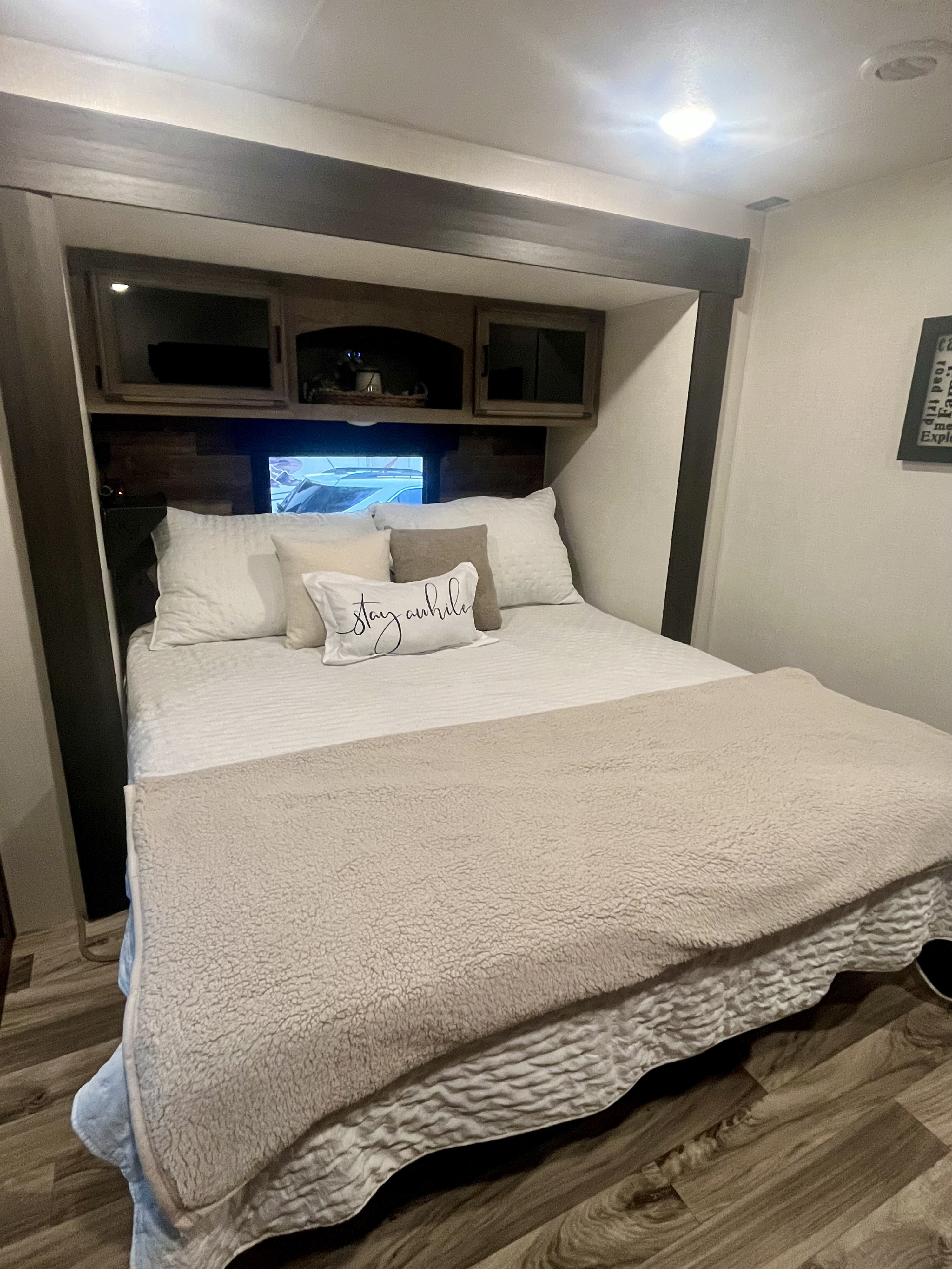 Cozy RV rental bedroom featuring a comfortable bed with a "Stay awhile" pillow, built-in storage, and warm lighting.. Sport Trek Touring Edition 2024