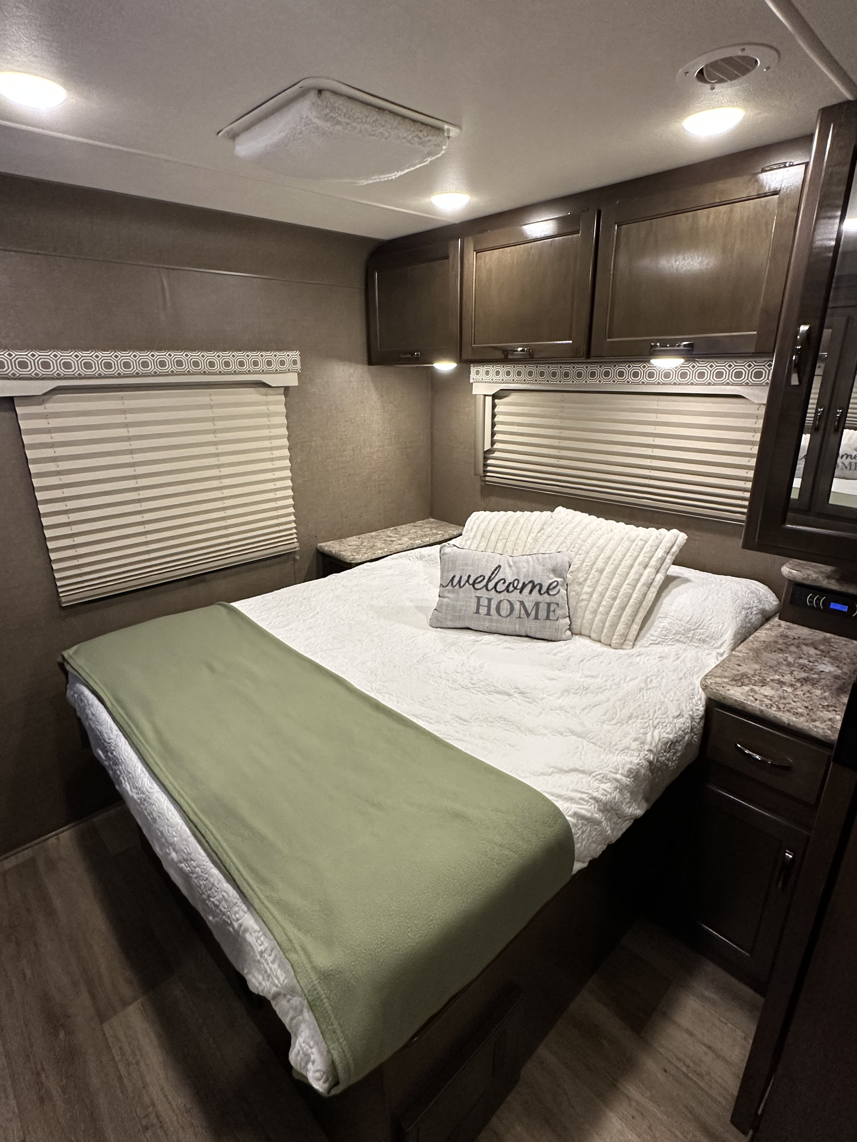 RV rental's inviting bedroom: white comforter, sage green blanket, "Welcome HOME" pillow, and ample overhead storage.. Thor Four Winds 2018