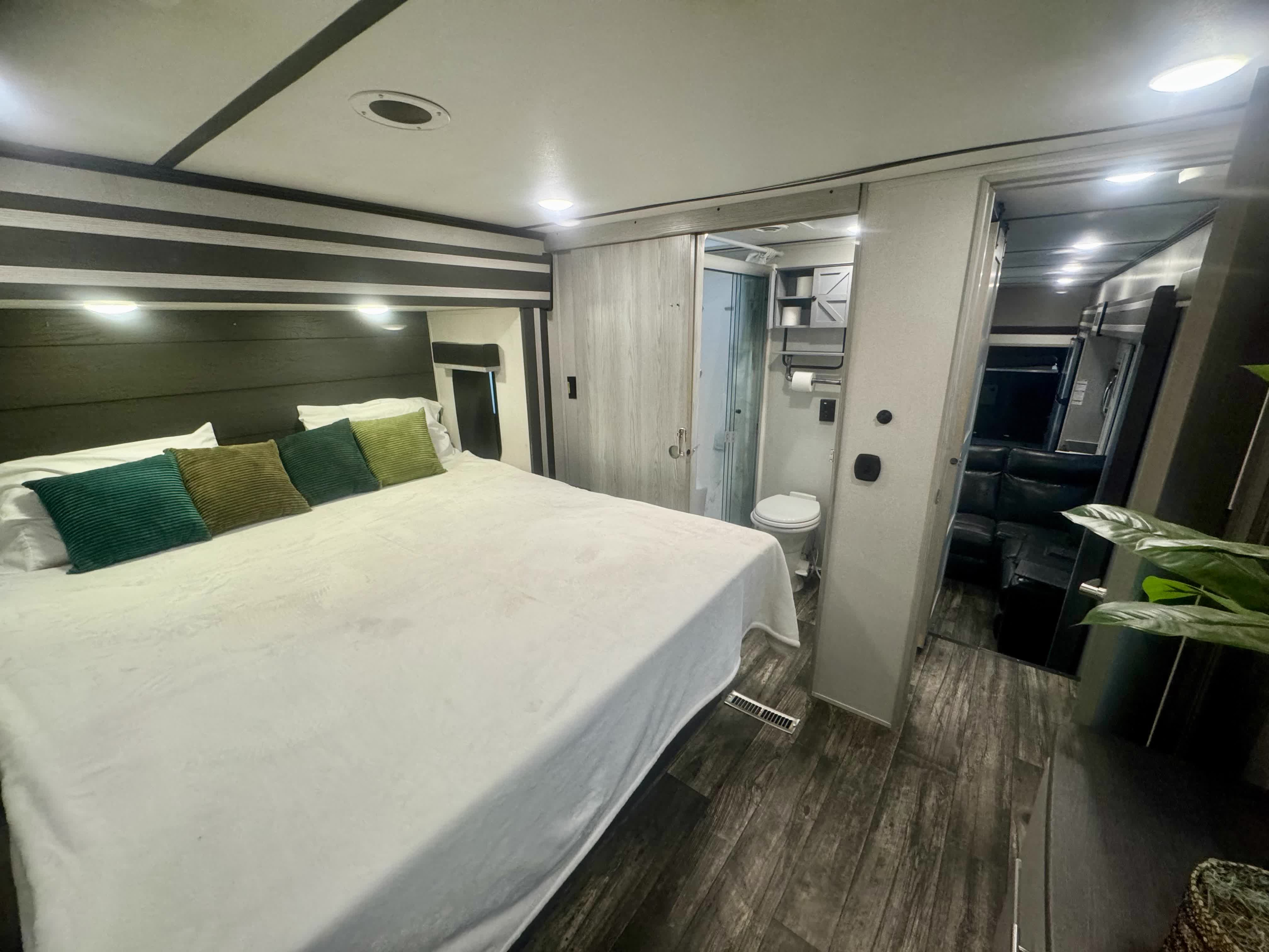 This modern RV rental features a spacious bedroom with a large bed, green pillows, and an attached bathroom. Living space is visible ahead.. Keystone Fuzion 2022