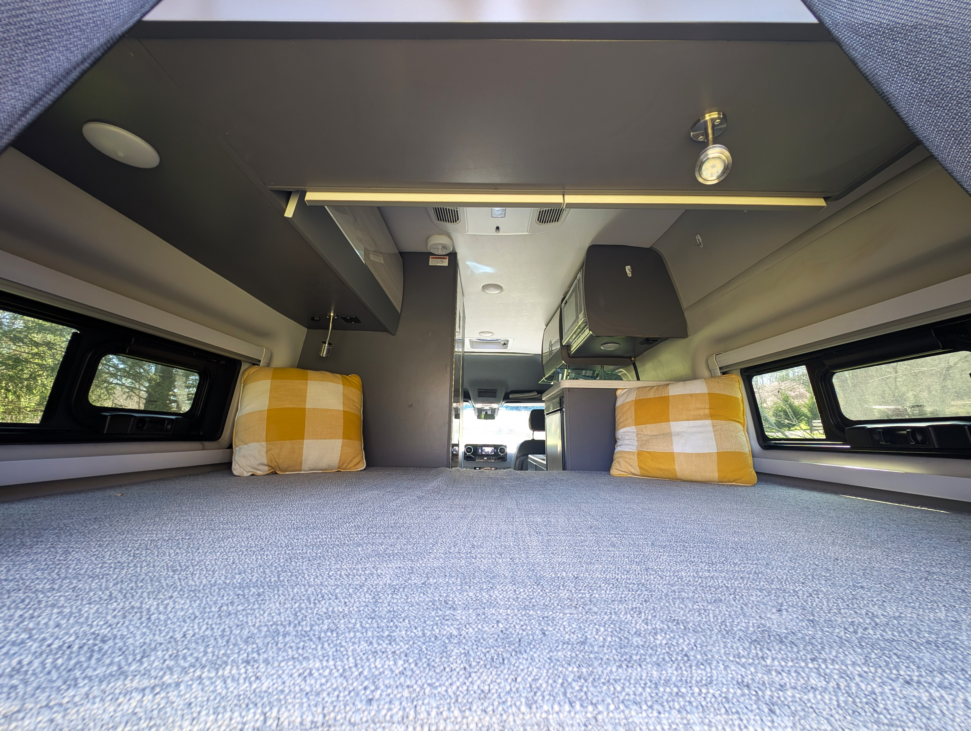 Spacious RV rental camper van interior. View from the large bed shows overhead storage, windows, and a compact kitchen.. Thor Sanctuary 2021