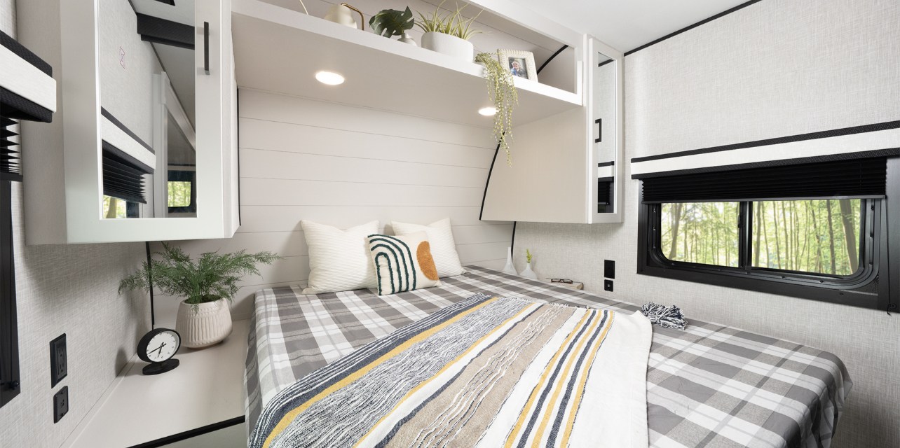 This RV rental's inviting bedroom offers plaid bedding, minimalist decor, and practical storage, creating a cozy travel space.. Jayco Jay Flight 261BHS 2025