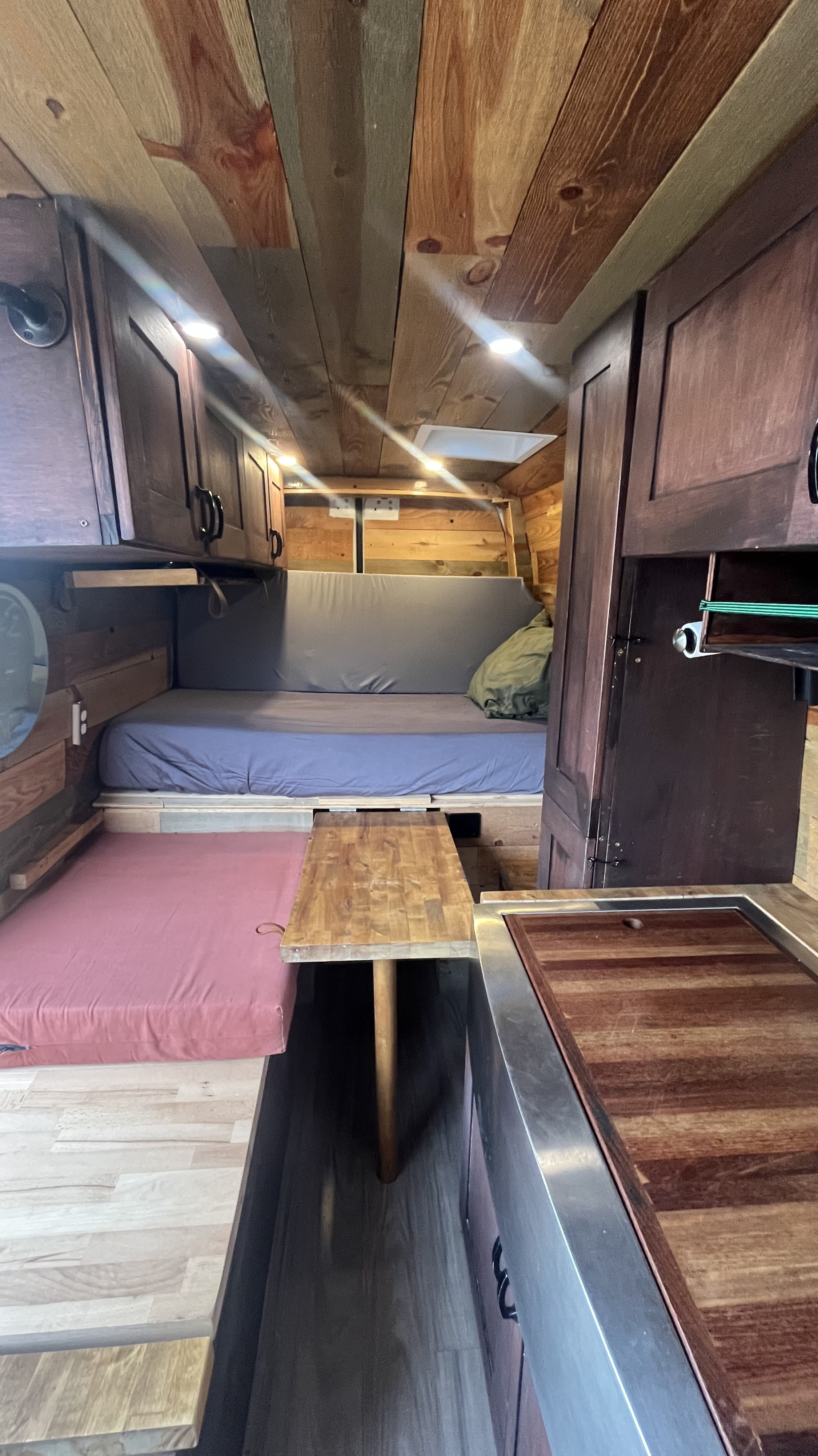 Cozy RV rental interior: wood-paneled walls, bed, dinette with pink cushion, and compact kitchen.. Mercedes-Benz Sprinter 2019