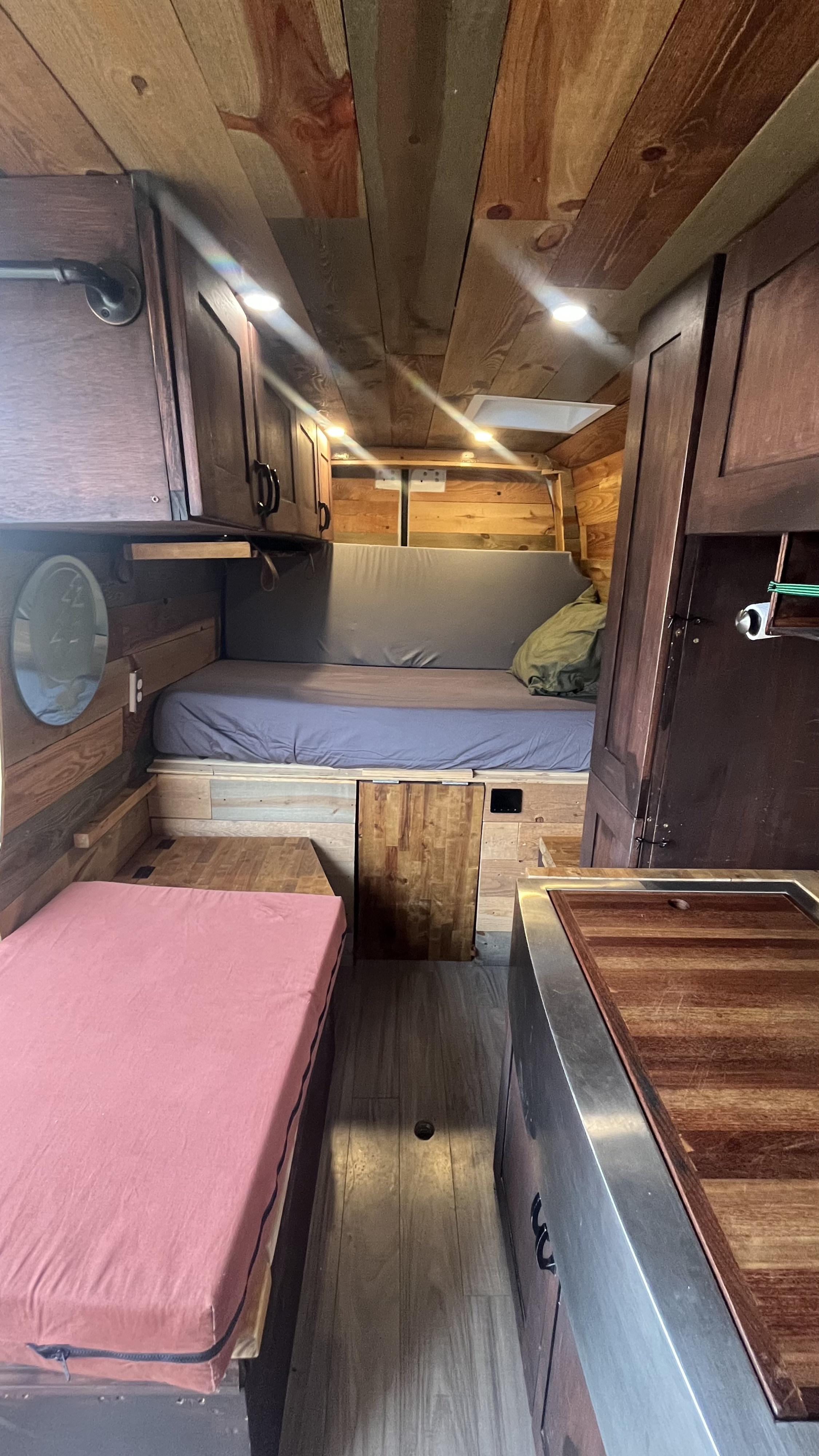 Explore this rustic RV rental interior with wooden paneling, a cozy bed, and functional kitchen space.. Mercedes-Benz Sprinter 2019