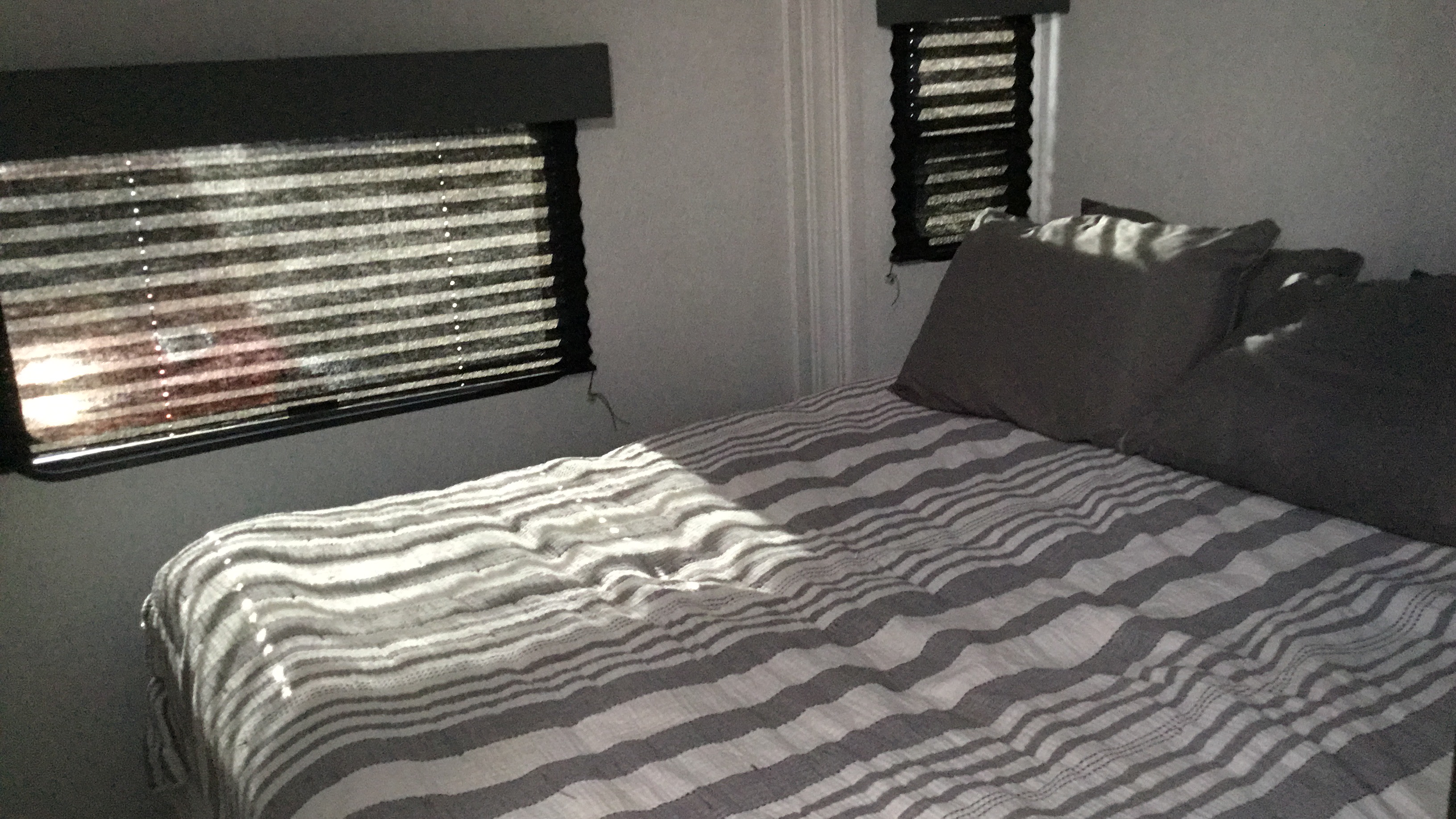 RV rental bedroom featuring striped bedding and sunlight through pleated blinds, creating a serene space for travel.. East to West Entrada 2950OK 2024