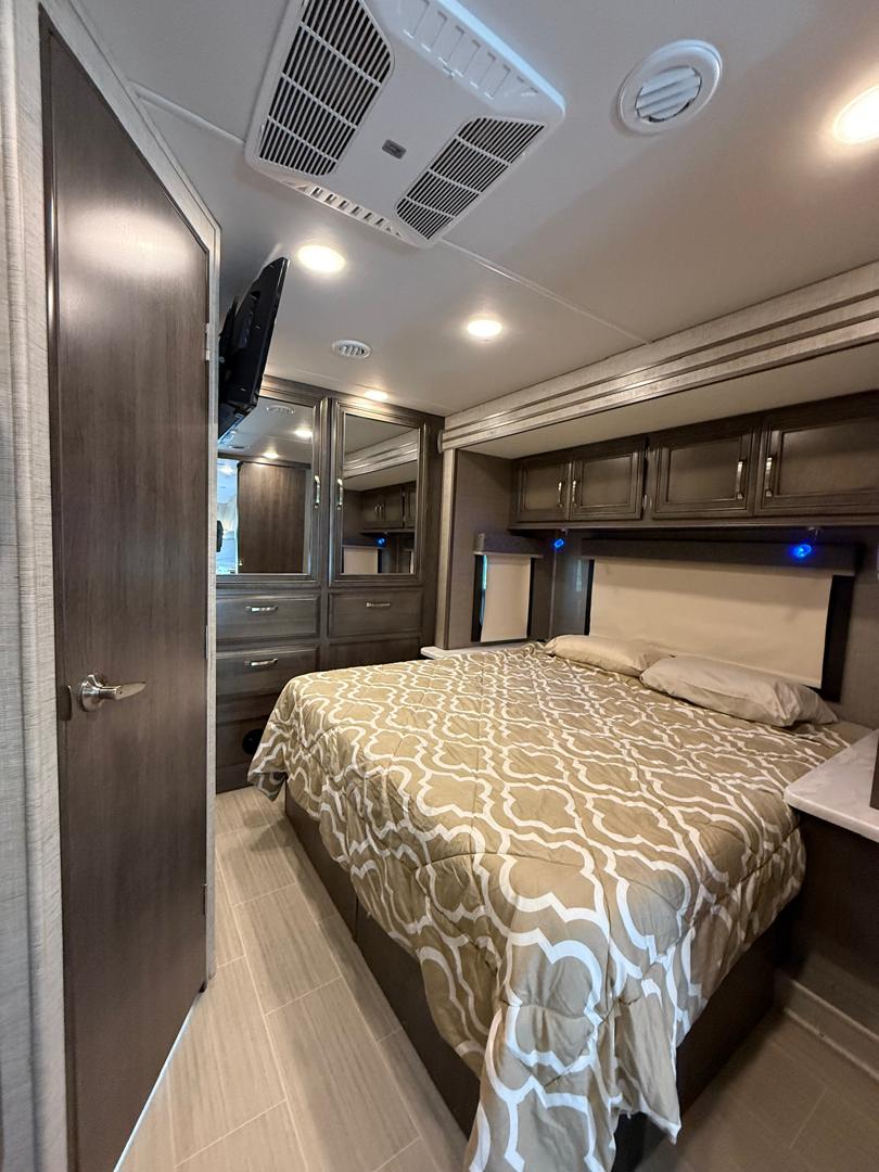 Inside an RV rental: a modern bedroom featuring a patterned bed, built-in storage, TV, and ceiling AC unit.. Forest River Entegra Esteem Jayco 2024