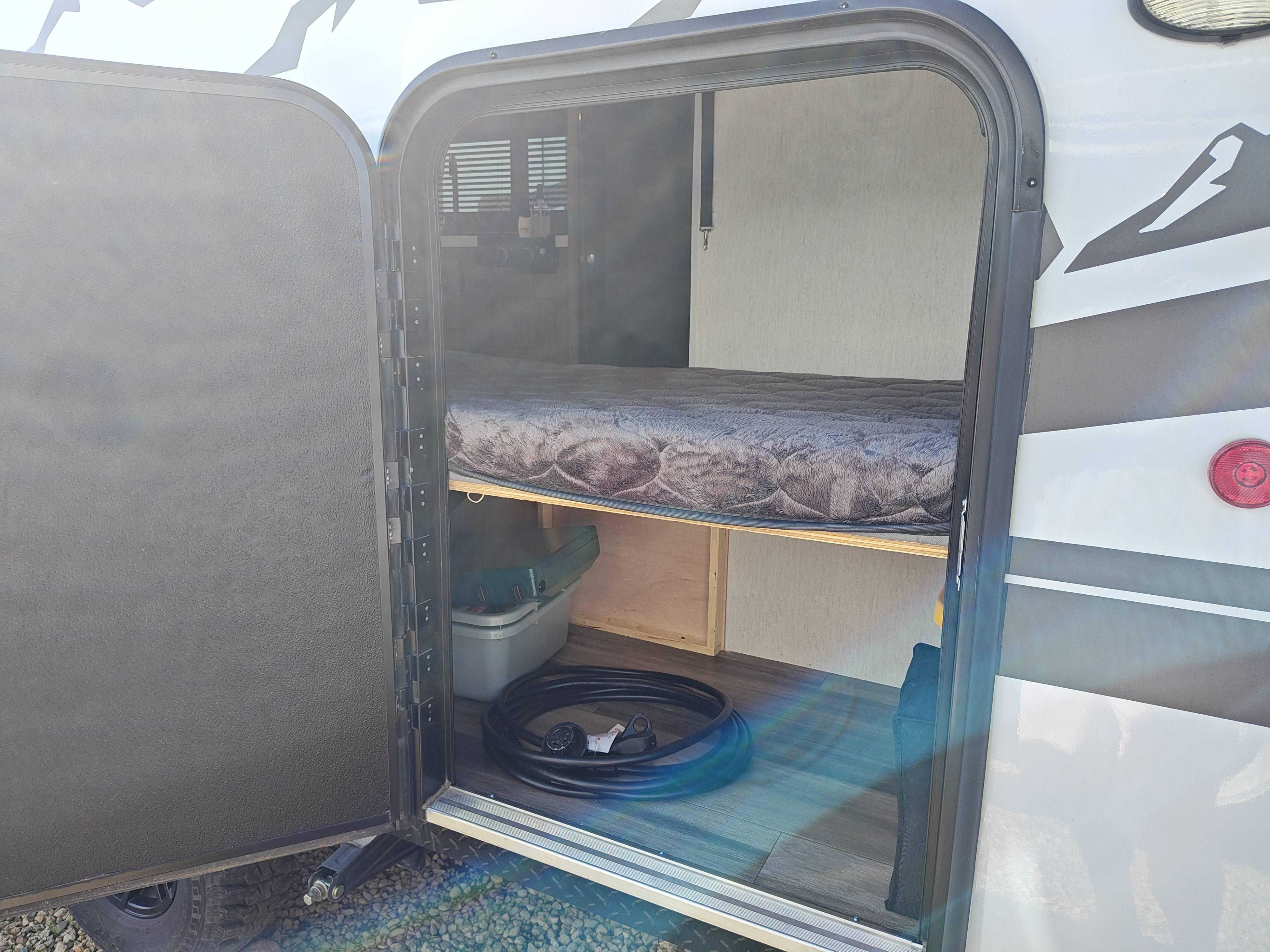 Inside an RV rental: a cozy bed above storage with a portable stove and hose, ready for your camping adventures.. Forest River Cherokee Cherokee Black Label Series 2023