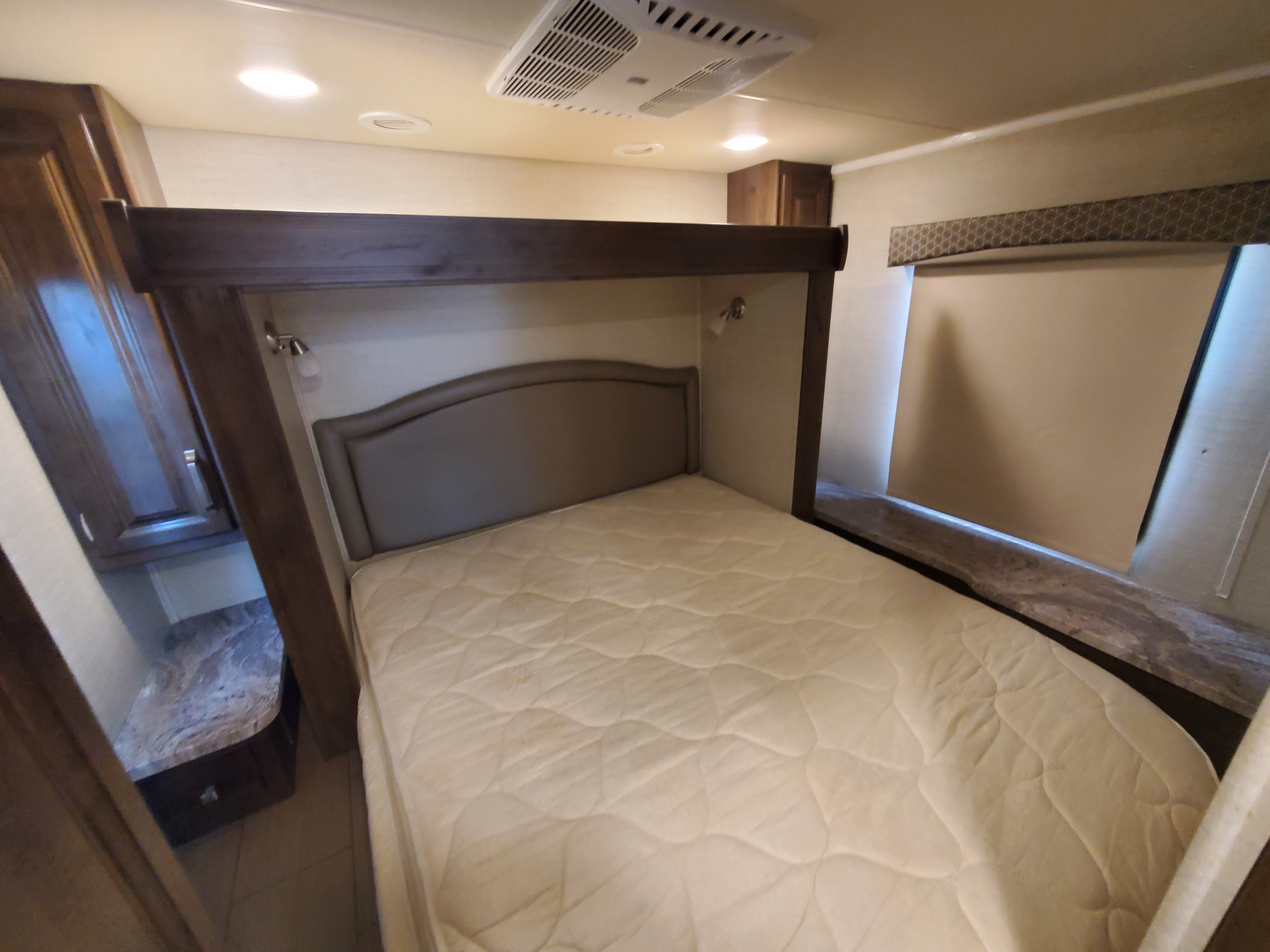RV rental bedroom: A clean, quilted mattress and headboard, with a small cabinet and window for a restful journey.. Jayco Greyhawk 2019