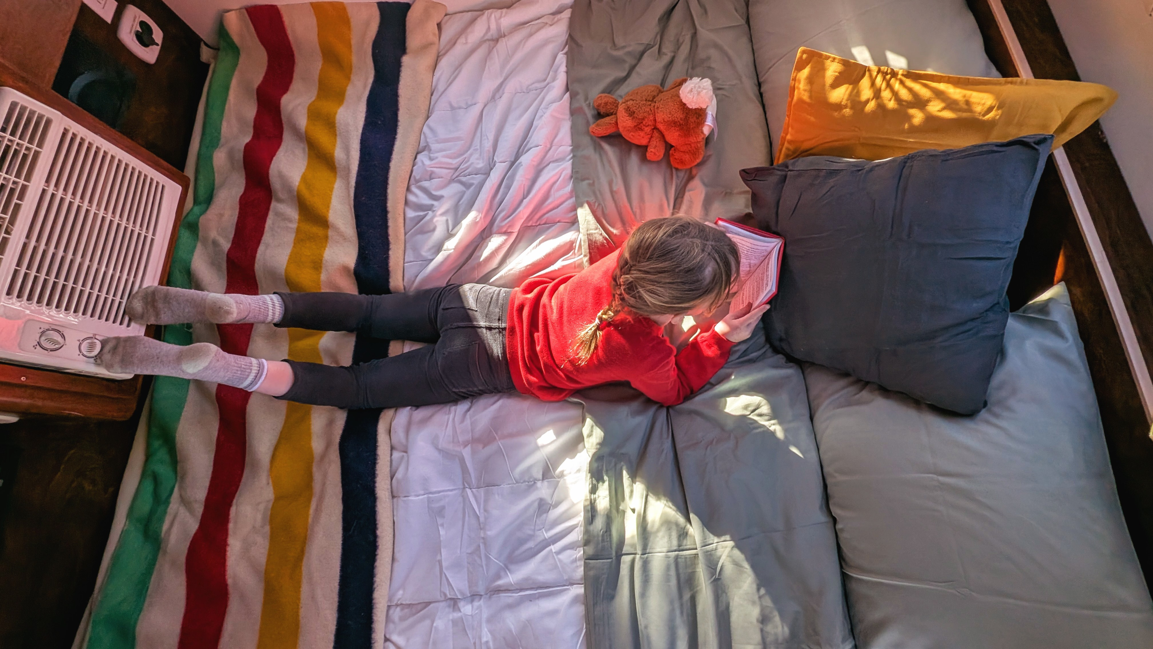 Cozy RV rental: A person reads a book on a bed with striped and grey bedding, an AC unit nearby.. T@G XL 2017