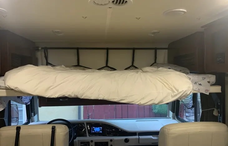 Spacious cab-over bed with white bedding inside an RV rental, positioned above the driver's area. Features a safety net.. Fleetwood storm 32A 2018