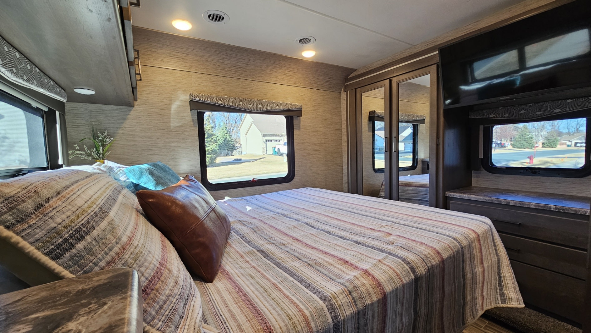 This comfortable RV rental bedroom features a striped bed, mirrored wardrobe, and TV, offering a cozy space for your travels.. Thor Four Winds 2023