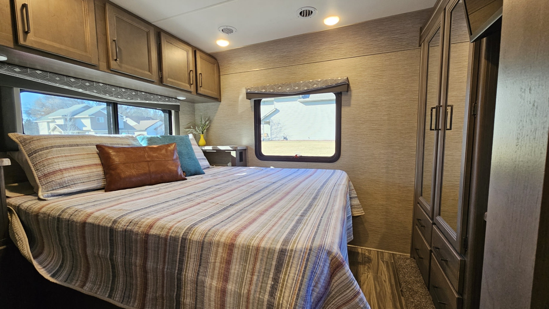 Comfortable RV rental bedroom with striped bedding, ample storage, and scenic windows, perfect for your next adventure.. Thor Four Winds 2023