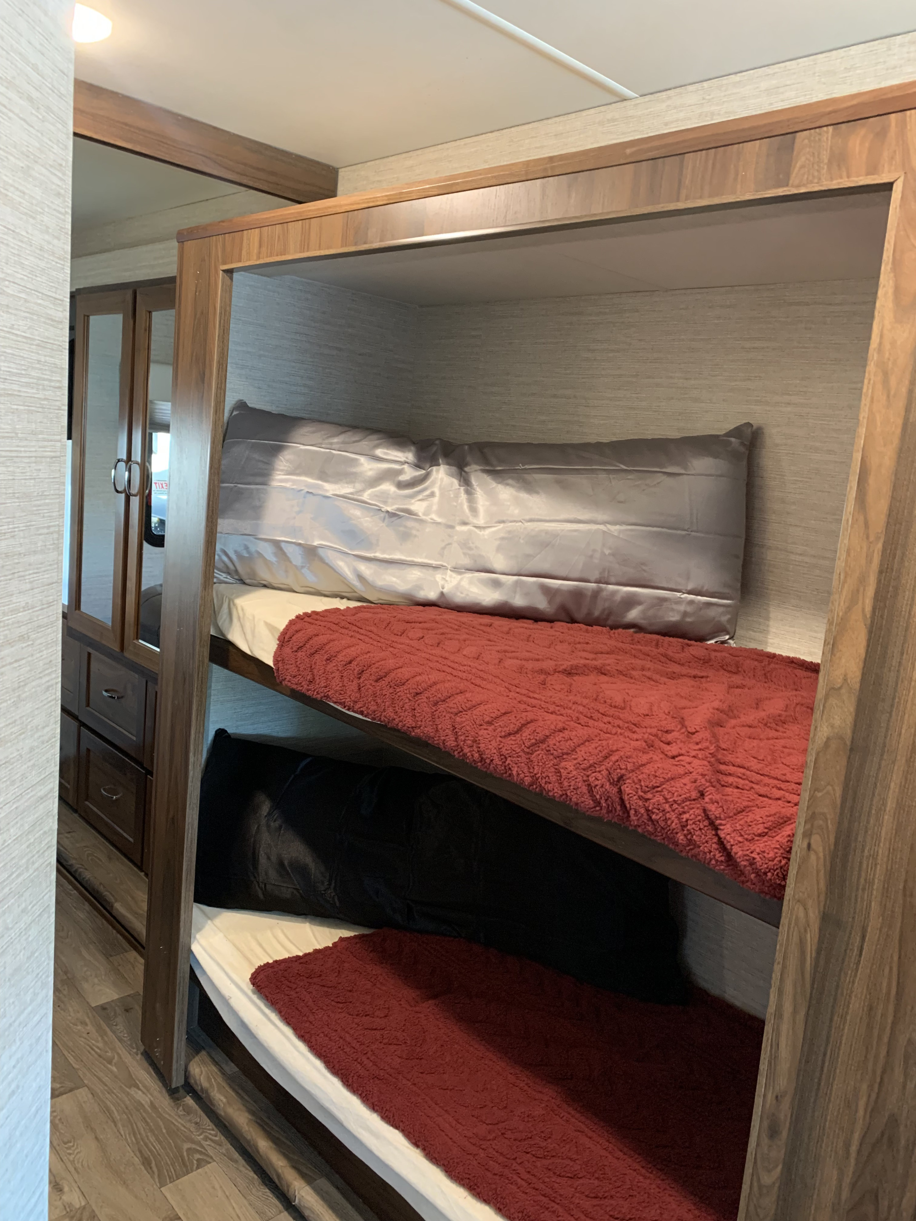 Interior of an RV rental with two bunk beds and a mirrored closet. Top bunk has gray bedding, bottom has red. Wood accents.. Winnebago Intent 2020