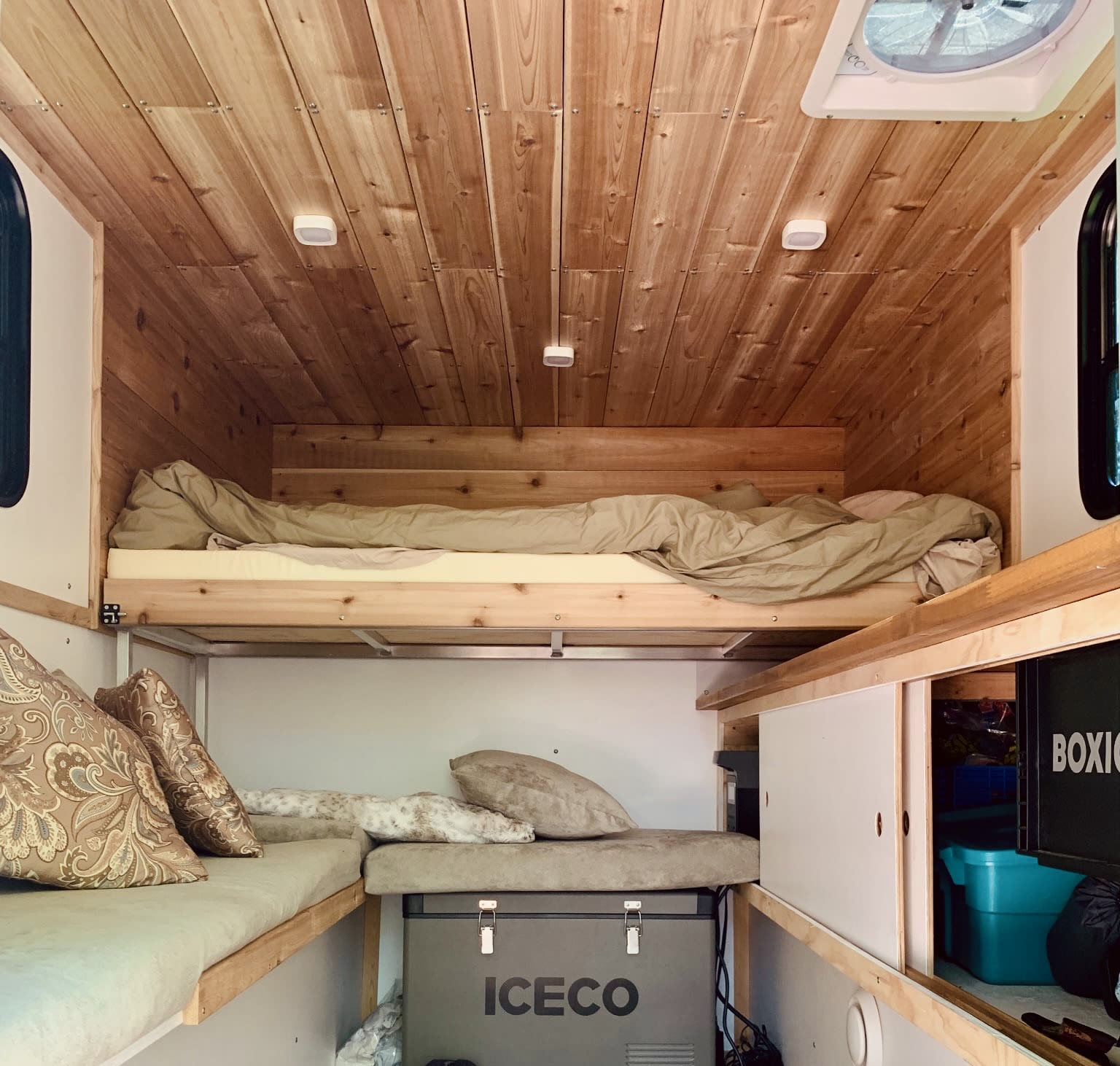 Cozy RV rental interior: wooden walls/ceiling, bunk beds, lower seating, cooler, & storage for comfort.. Custom Camper 2024