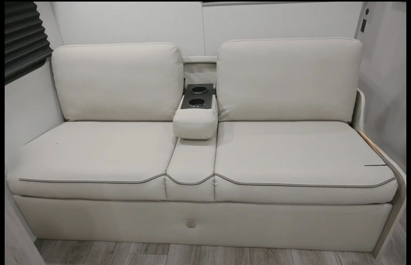 Comfortable, cream two-person RV sofa with flip-down armrest and cup holders, ideal for an RV rental interior.. Coachmen Catalina 2025