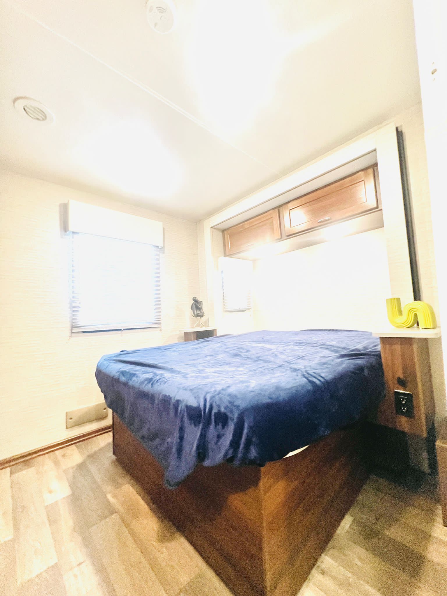 Cozy RV rental bedroom with a comfy blue bed, window, and overhead storage cabinets, ideal for travelers.. Winnebago Outlook 2020