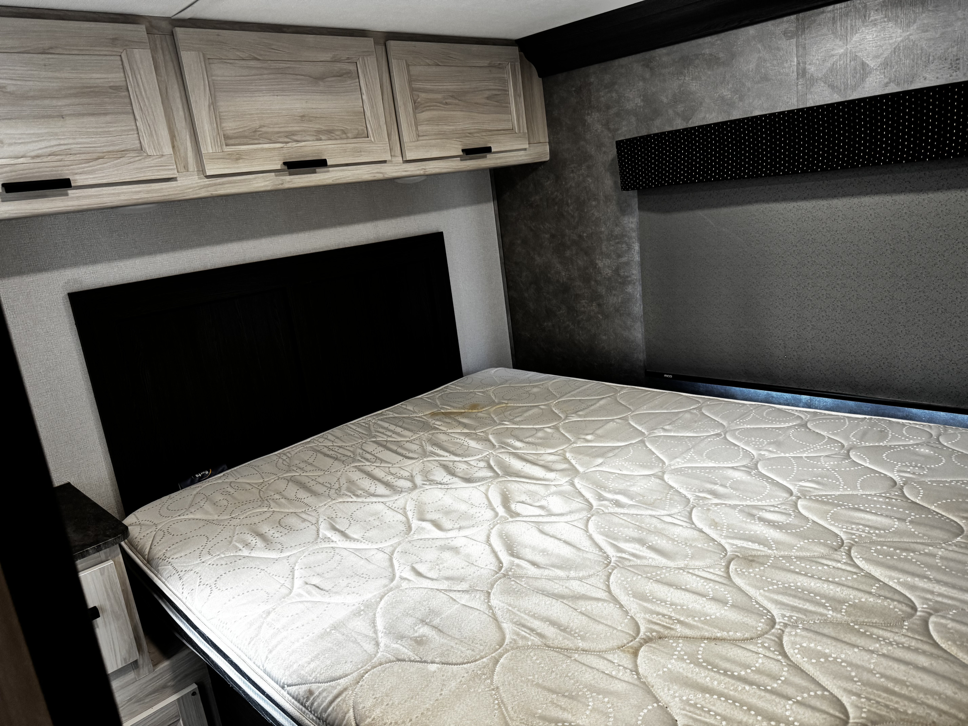 RV rental bedroom with a white mattress (stained), black headboard, wood cabinets, and textured walls.. Forest River Forester 2022