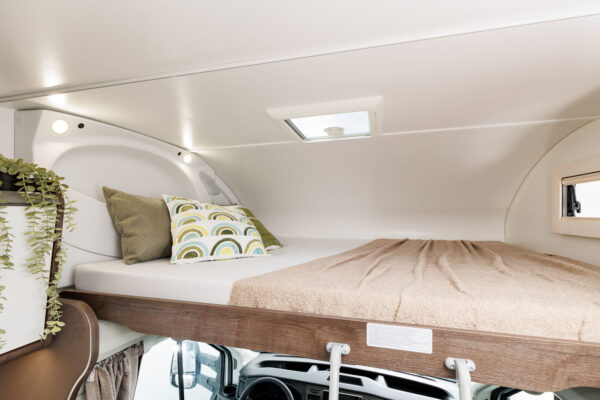 The cozy interior of an rv rental, showcasing an inviting overhead bed with pillows and a blanket, lit by ceiling lights and a skylight.. Benimar Sport 324 UP 2025