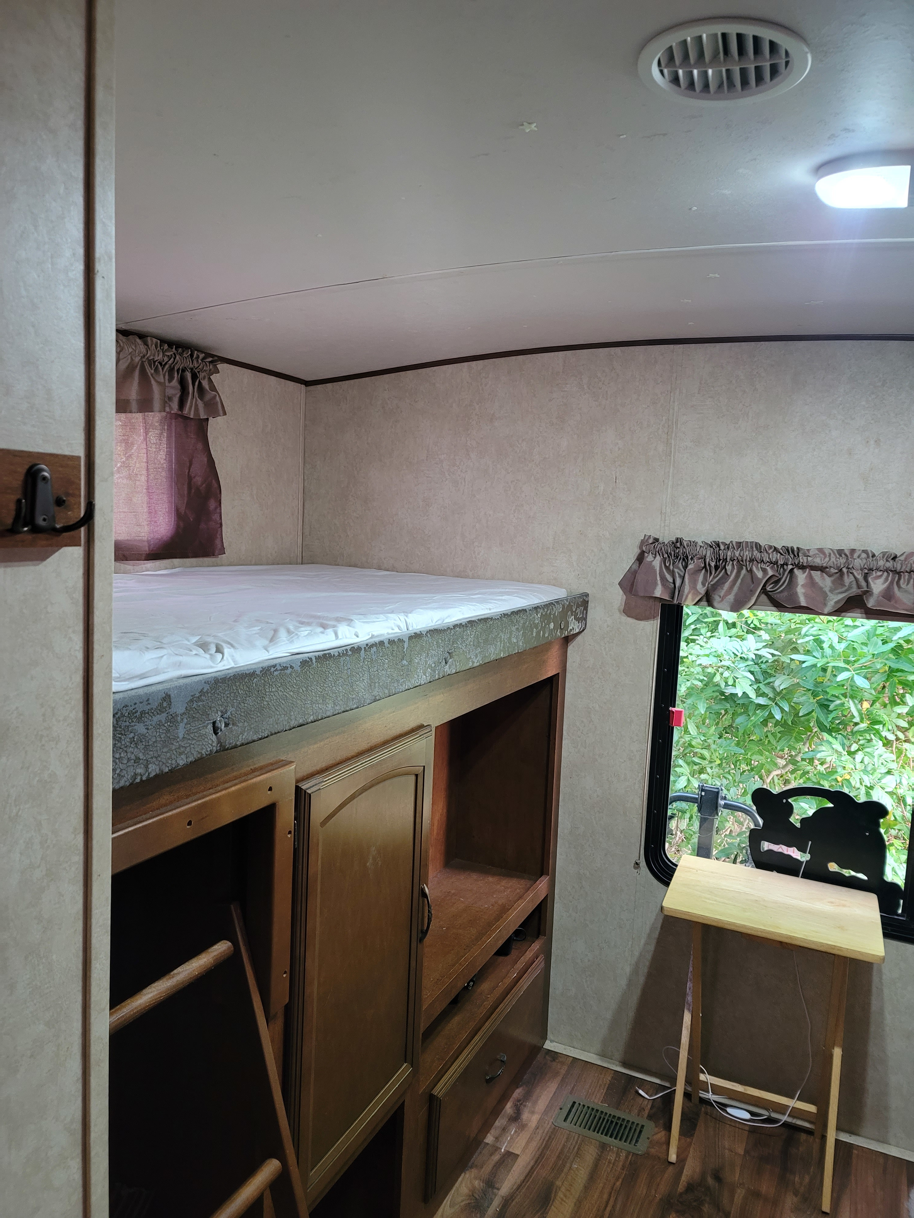 RV rental interior featuring a bunk bed with a white mattress, wooden storage unit, ladder, and a window with green outdoor view.. Forest River Wildwood Heritage Glen Lite 2014