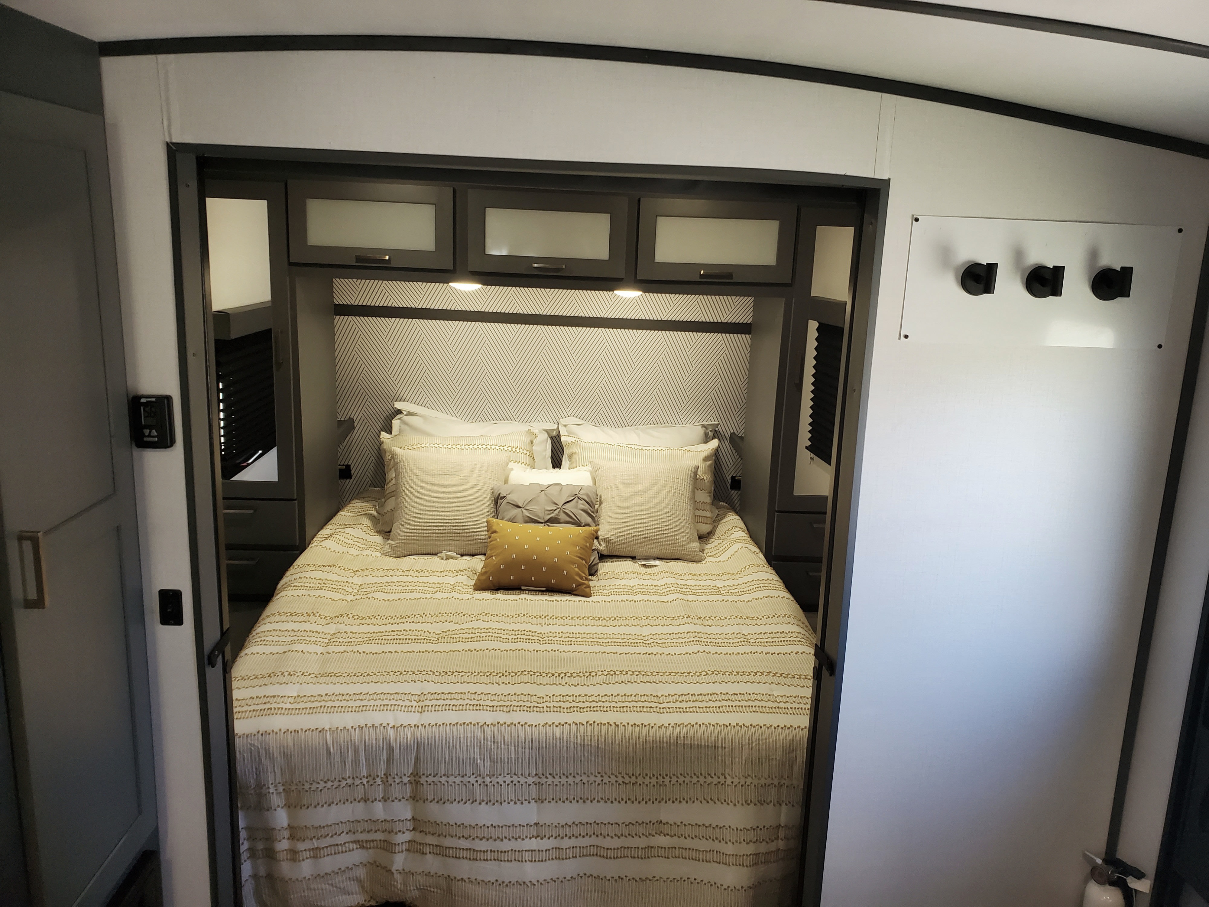 Inside an RV rental, this bedroom features a bed with decorative pillows, overhead storage, and a thermostat for guests.. Keystone RV Bullet Ultra Lite 2023