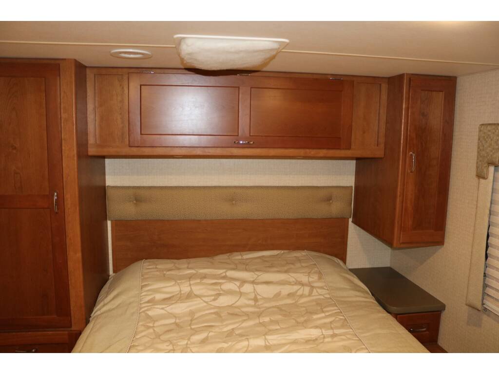 RV rental bedroom: Bed with padded headboard, wood cabinets, and side table, providing a functional, cozy space.. Winnebago Minnie Winnie 2017