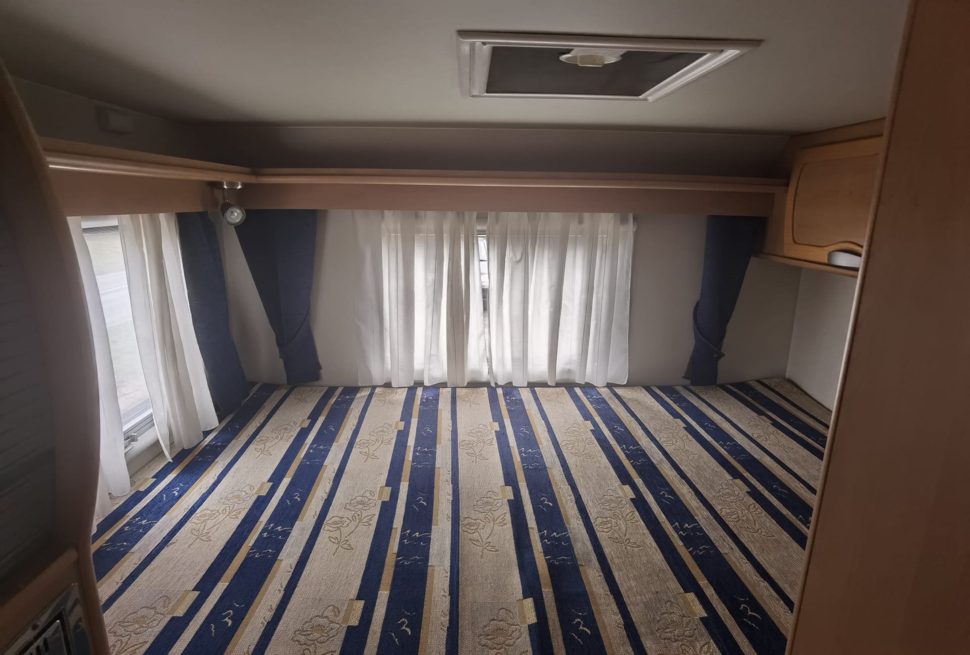 Inside your next rv rental: a cozy sleeping area with patterned floor, white curtains, and overhead cabinet.. FIAT McLouis Glen 690g 2005
