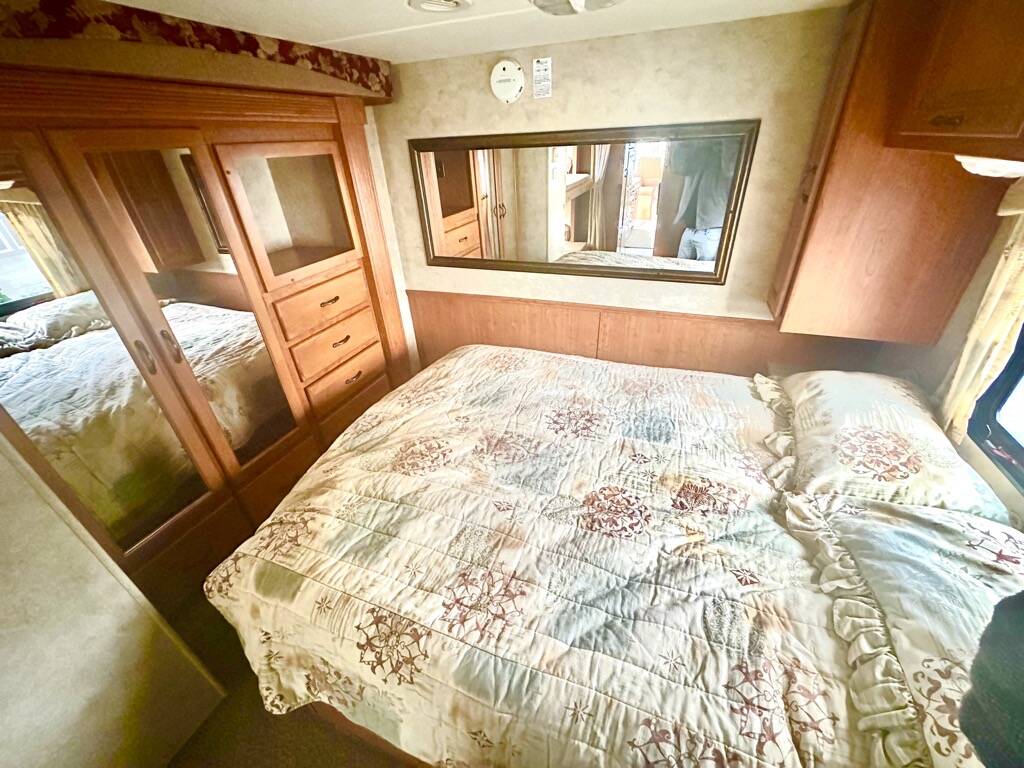 Cozy RV rental bedroom: A patterned bedspread, mirrored wardrobe with drawers, and overhead storage optimize space in this camper.. Damon Corporation Challenger 2008