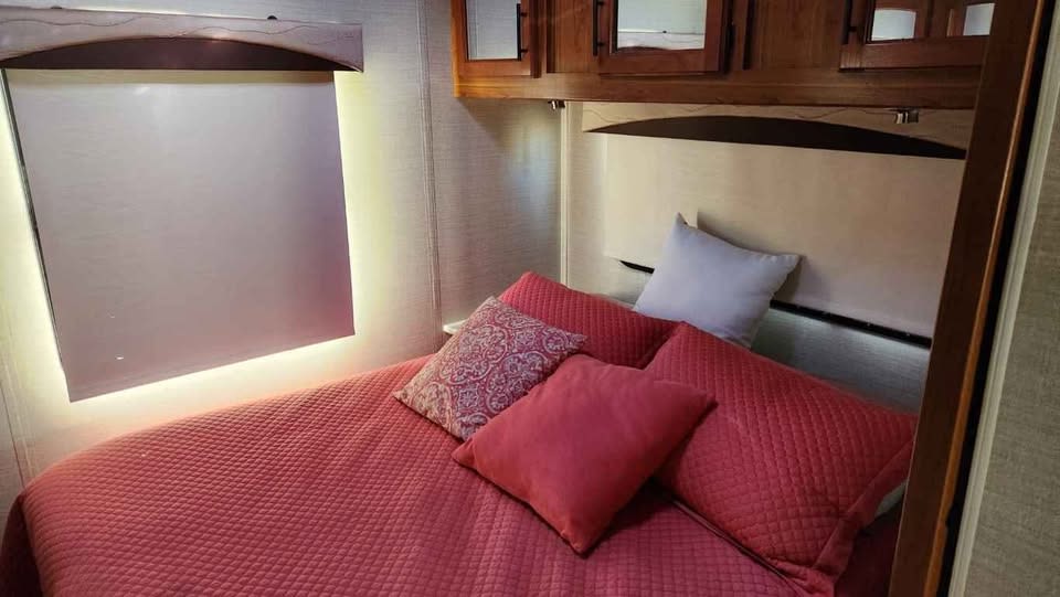 Experience comfort in this RV rental's inviting bedroom, featuring a plush bed with red bedding and accent lighting.. Jayco Greyhawk 2017