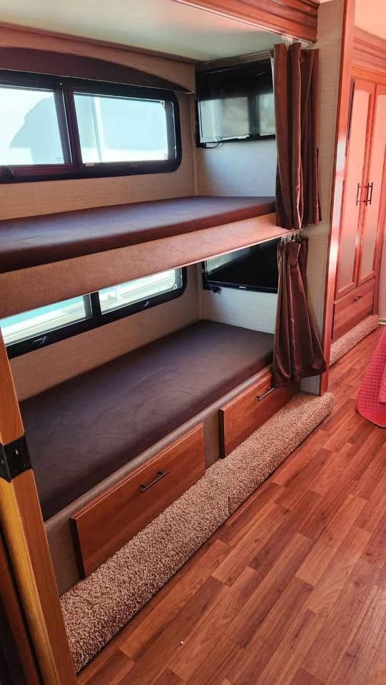 Spacious bunk beds in an RV rental, featuring windows, TVs, and storage drawers for comfortable travel.. Jayco Greyhawk 2017
