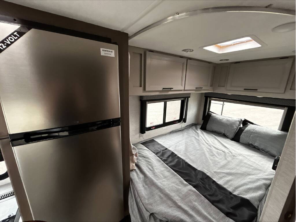 RV rental interior: A compact bedroom featuring a 12-volt refrigerator, bed, overhead cabinets, and windows.. GMC/THOR MAGNITUDE 2025
