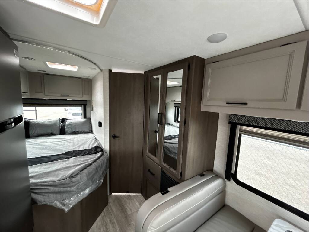 RV rental interior showing a comfortable bed with gray bedding, mirrored wardrobe, overhead cabinets, and a seating area.. GMC/THOR MAGNITUDE 2025