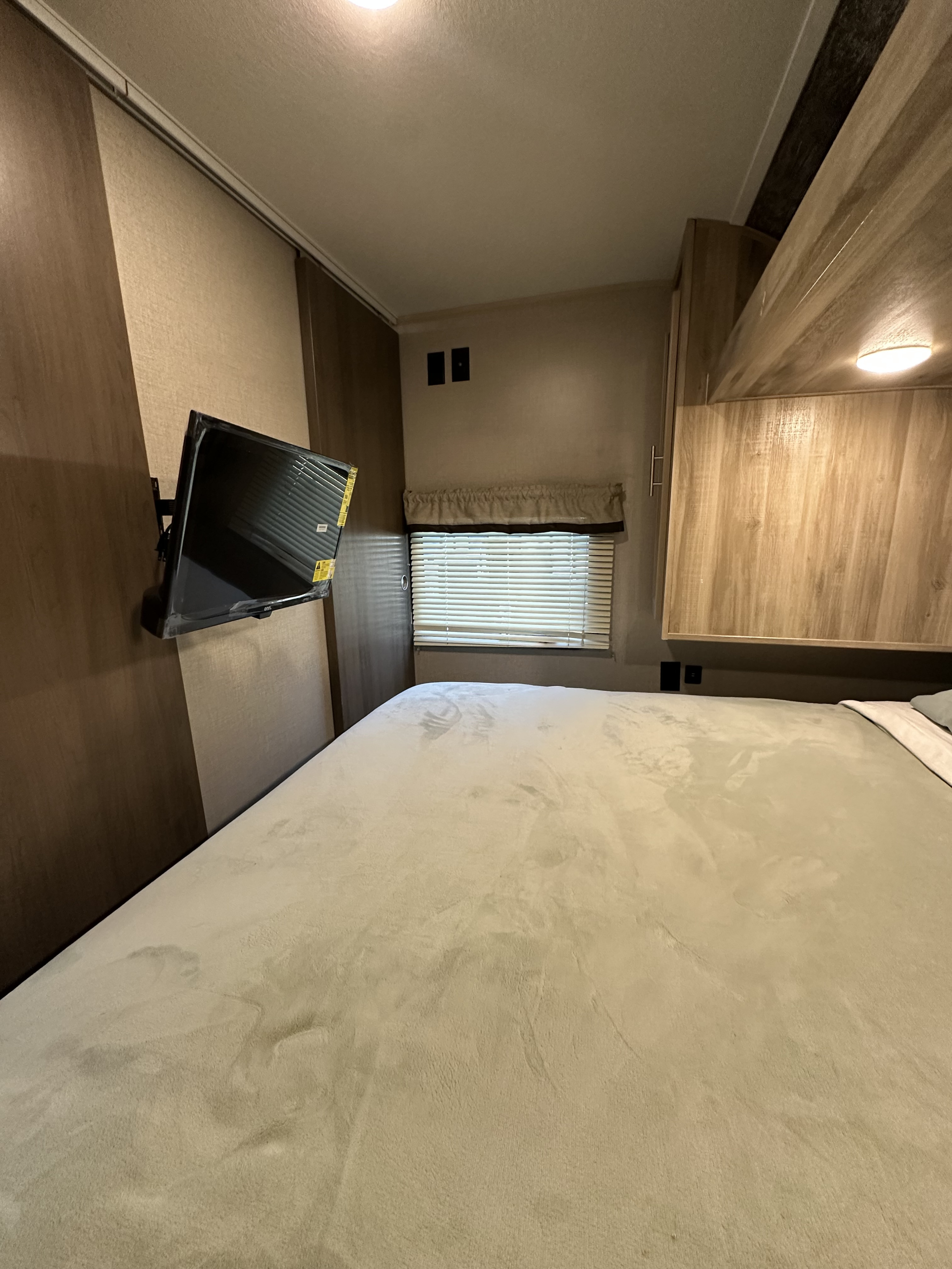 Cozy RV rental bedroom featuring a large bed, wall-mounted TV, window with blinds, and wood paneling.. Coachmen Catalina Summit 261BHS 2021