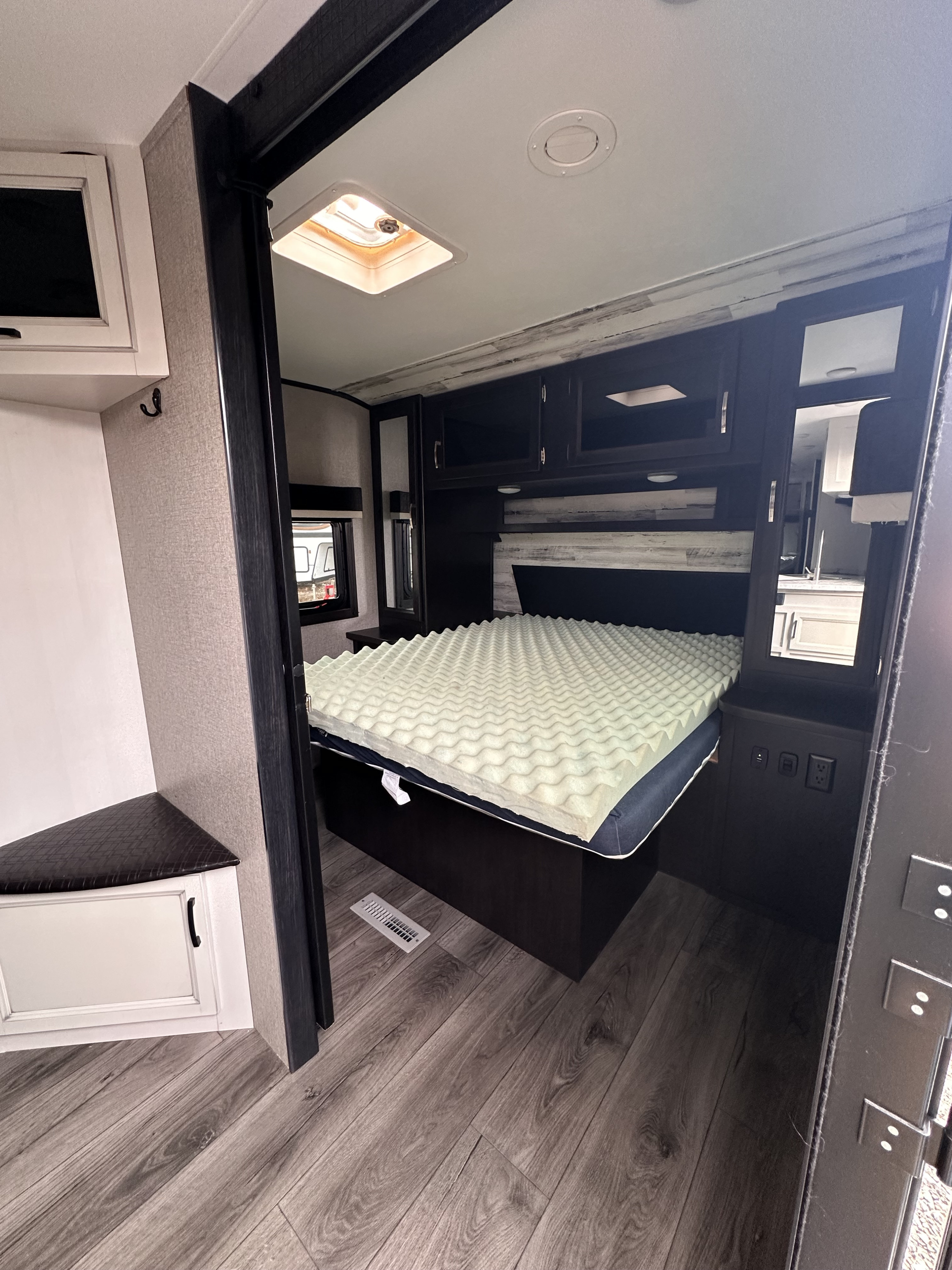 Cozy RV rental bedroom: modern space with bed, wavy foam topper, overhead cabinets, and wood-look flooring.. Jayco Jay Feather 2021