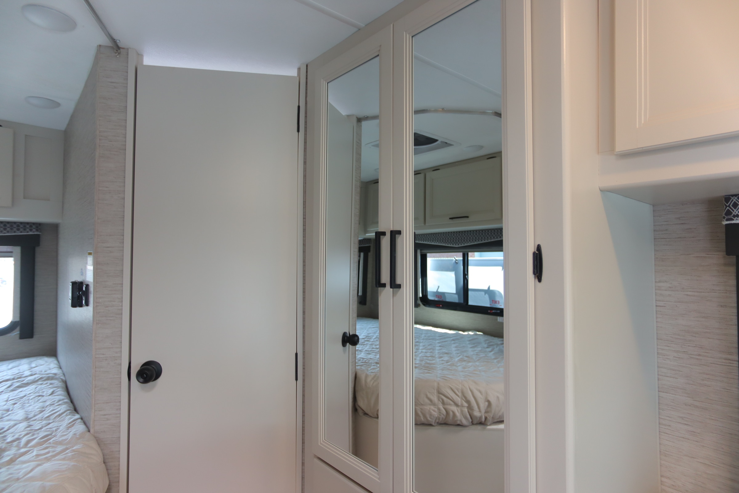 RV rental interior view: a mirrored wardrobe stands beside the bedroom doorway, reflecting the bed and window. Bright, modern space.. Thor Motor Coach Chateau 2024