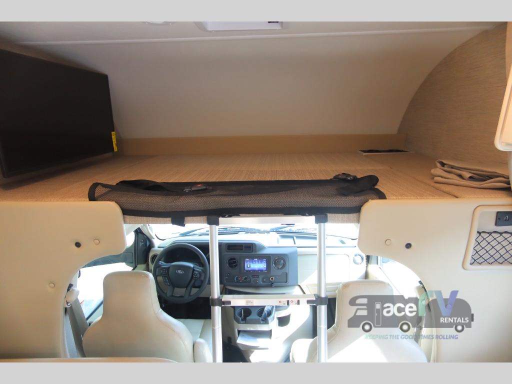 Inside an RV rental: a comfortable cab-over bunk bed with TV, overlooking the driver and passenger seats.. Thor Motor Coach Four Winds 2023