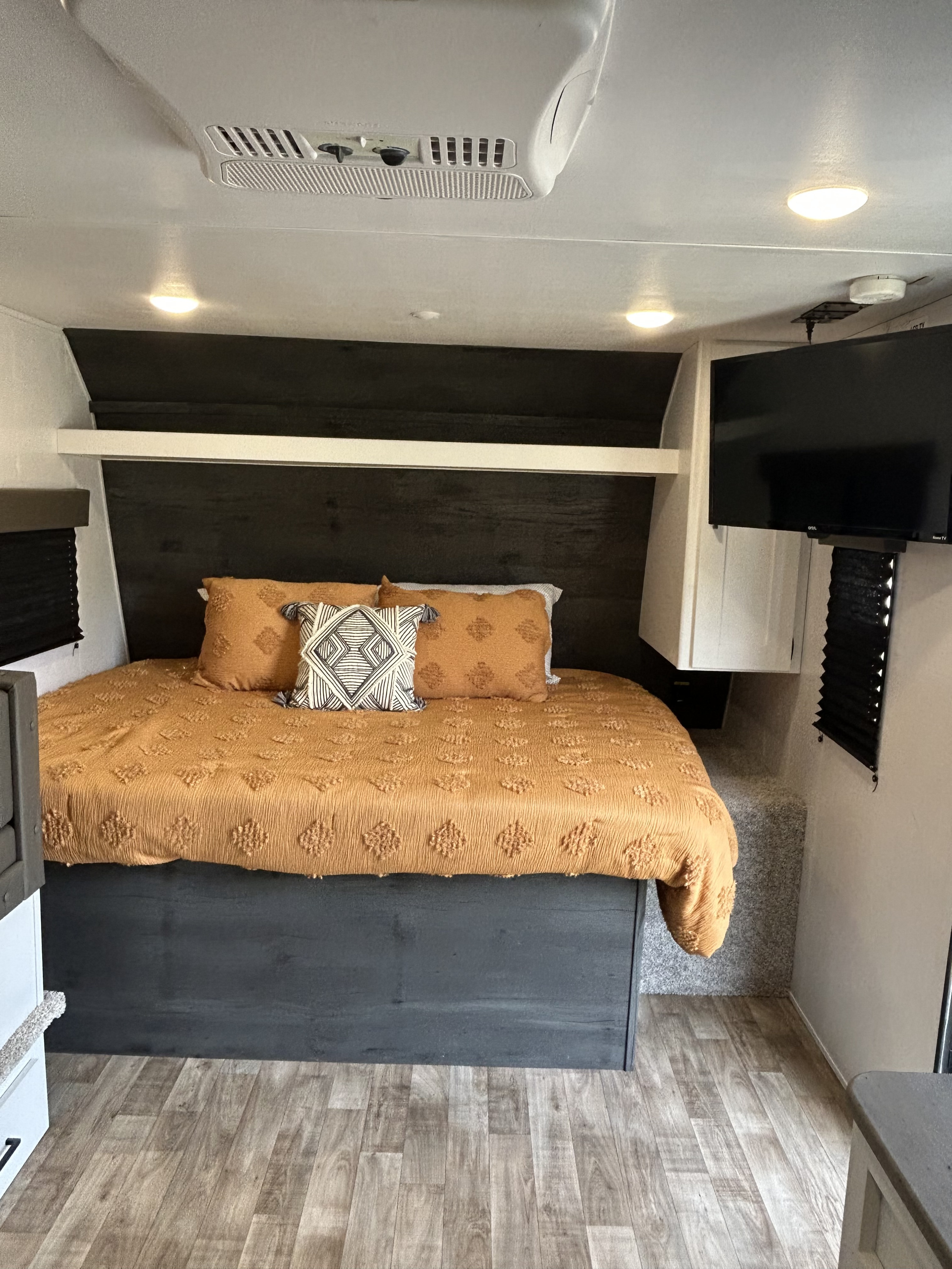 Spacious RV rental bedroom featuring a comfy bed with orange bedding, dark wood headboard, wall TV, and AC unit.. Keystone RV Hideout 2022