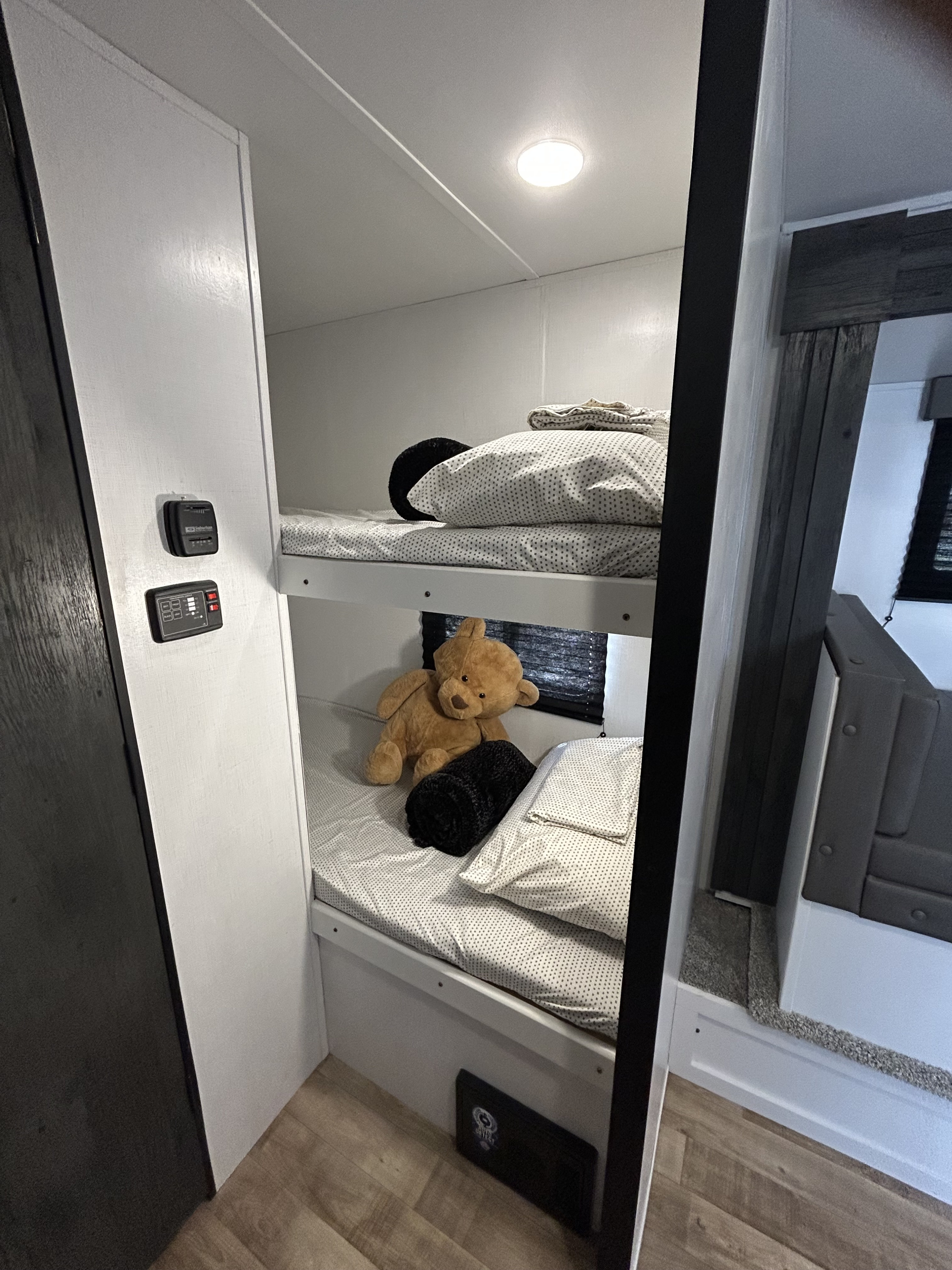 Inside an RV rental: two cozy bunk beds with bedding, a teddy bear, and controls on the wall.. Keystone RV Hideout 2022
