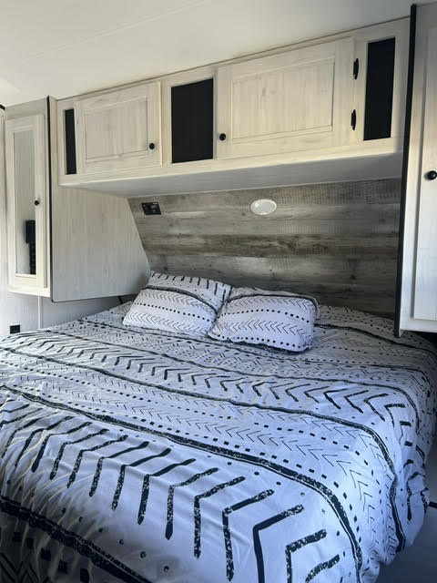 RV rental bedroom: Features a comfy bed with unique patterned bedding, overhead storage cabinets, and a rustic wood-paneled headboard.. Heartland Lithium 2021