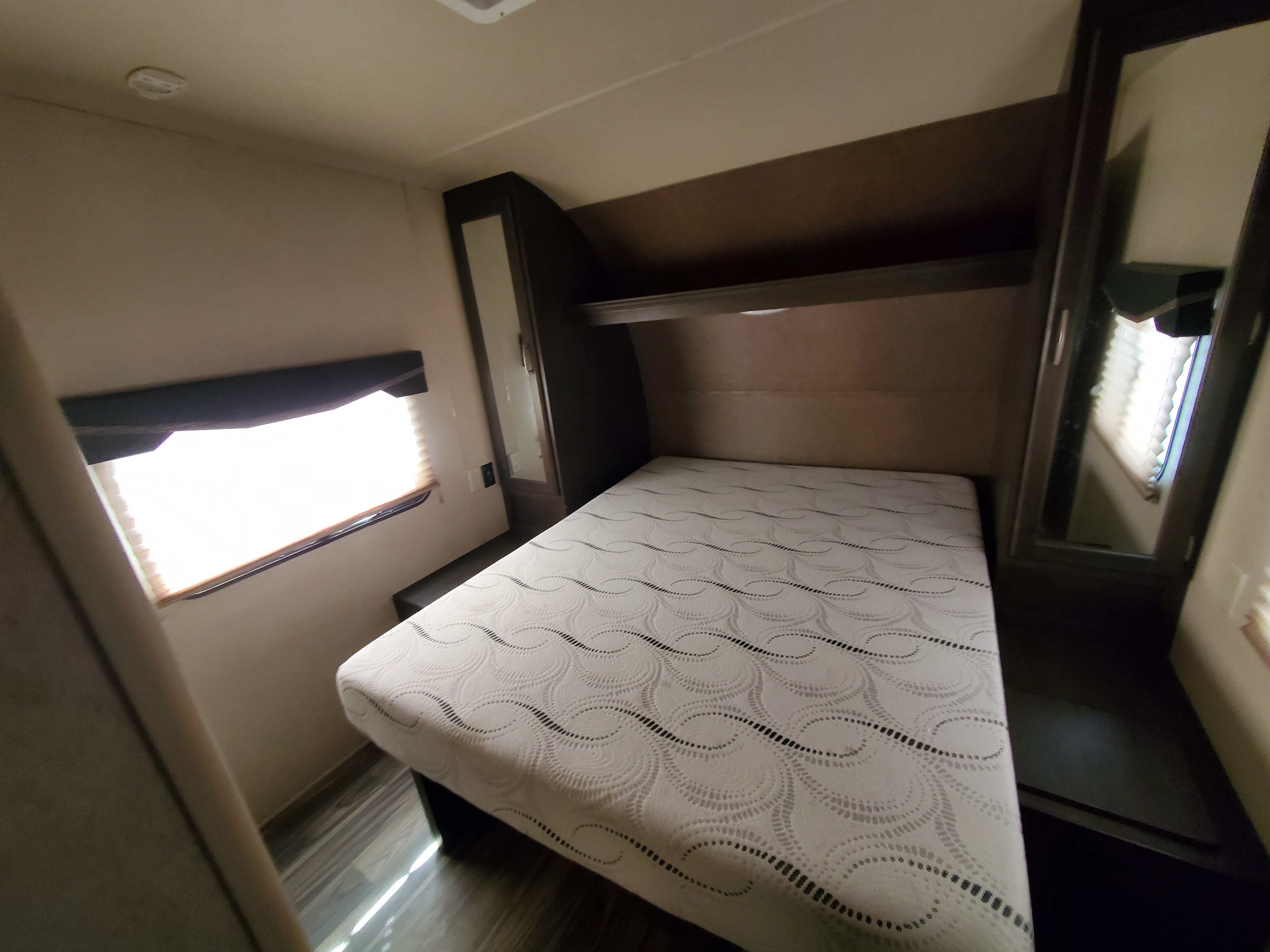 Cozy RV rental bedroom featuring a bed with a patterned mattress, window with blinds, and built-in storage/mirror.. Forest River Shockwave 2019
