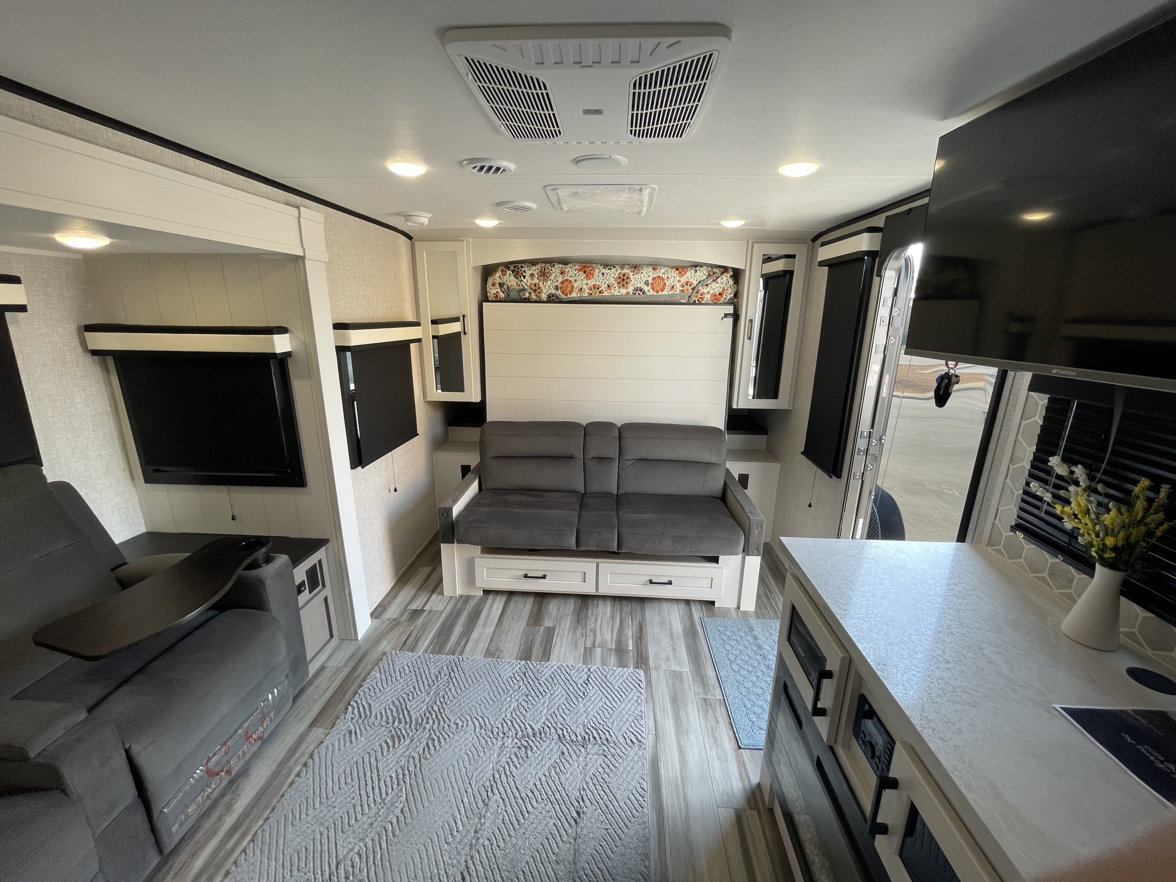 Spacious RV rental interior featuring a gray sofa, comfortable recliners, flat-screen TV, and modern kitchen area.. Jayco Jay Feather 2025