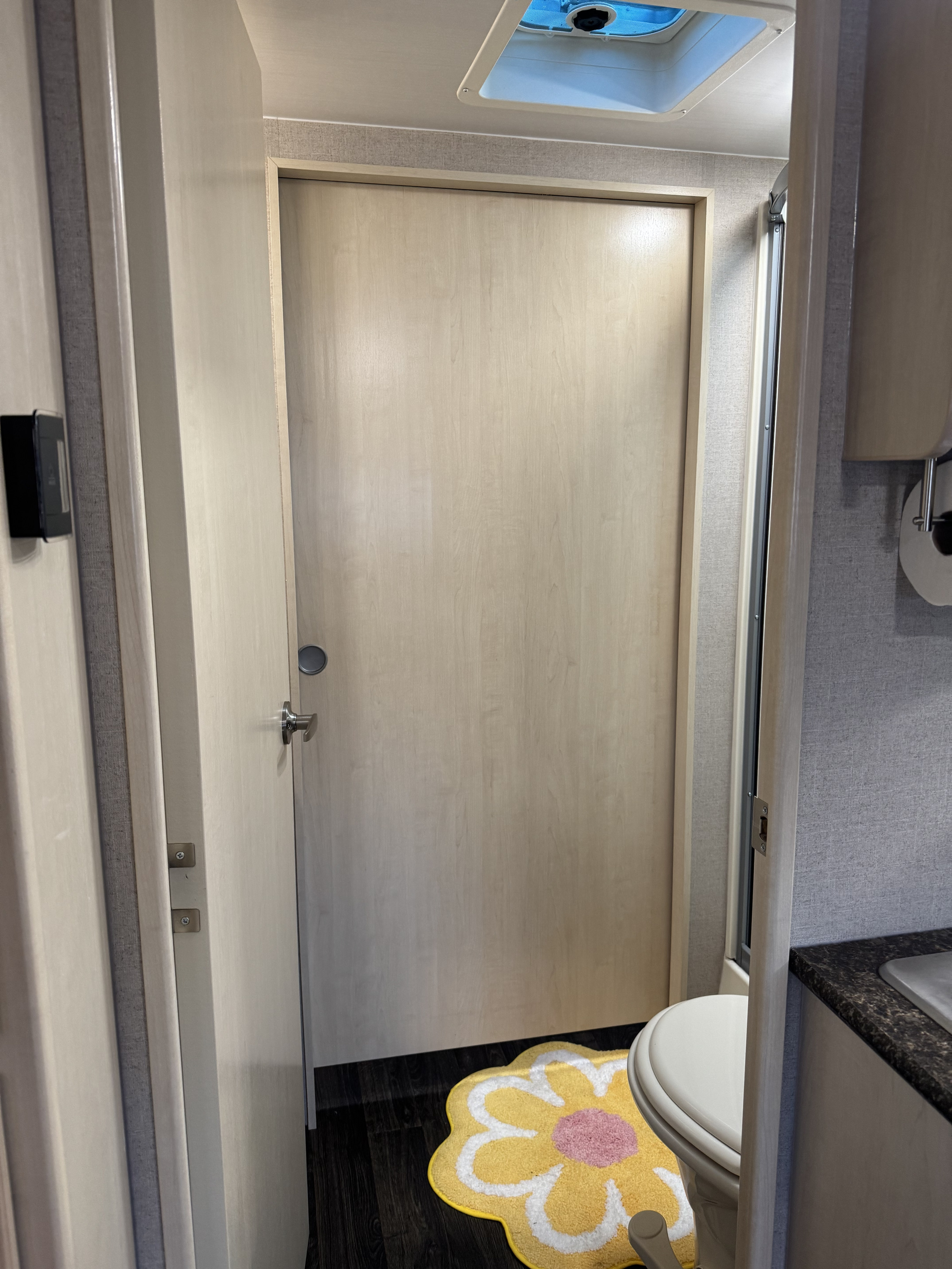 RV rental's light-wood bathroom door, with compact toilet & shower. A cheerful flower rug adds color.. Minnie Minnie Trailer 2019