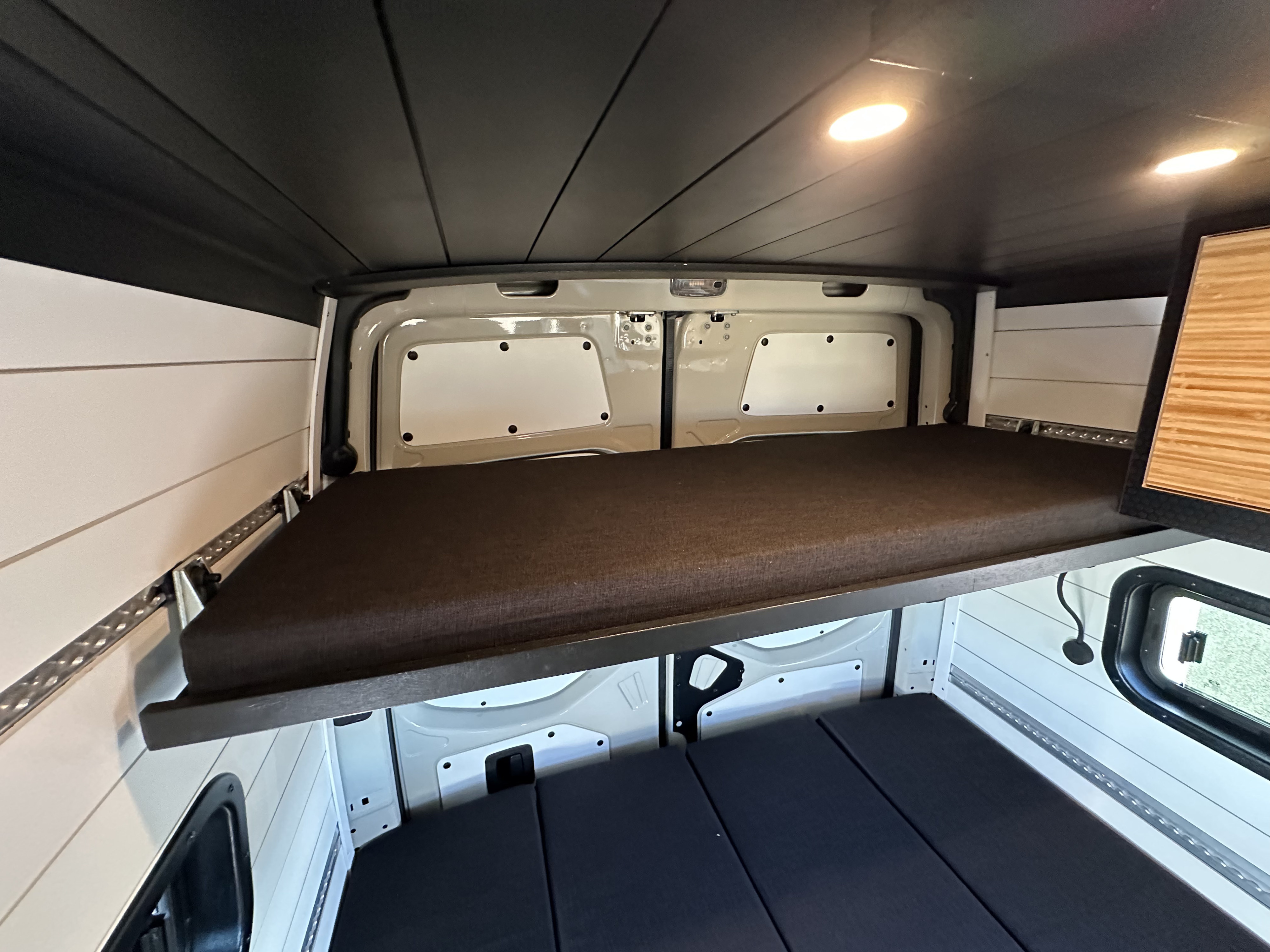 RV rental: Camper van interior showing an elevated bed, lower sleeping area, white paneled walls, and dark ceiling.. Mercedes-Benz Sprinter 2500 AWD 2024