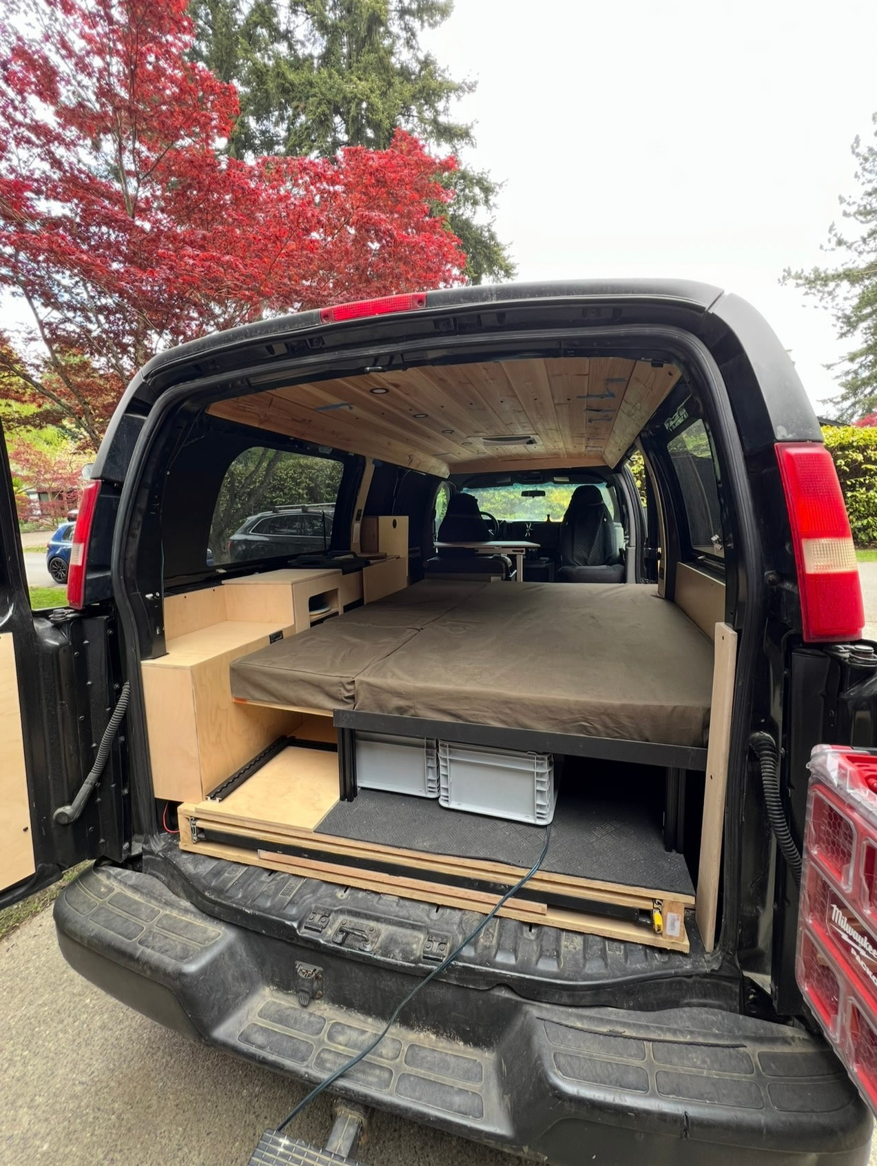 This converted camper van interior features a comfy bed, wood ceiling, & clever storage. Ideal for an RV rental adventure!. Chevrolet AWD Express 2003