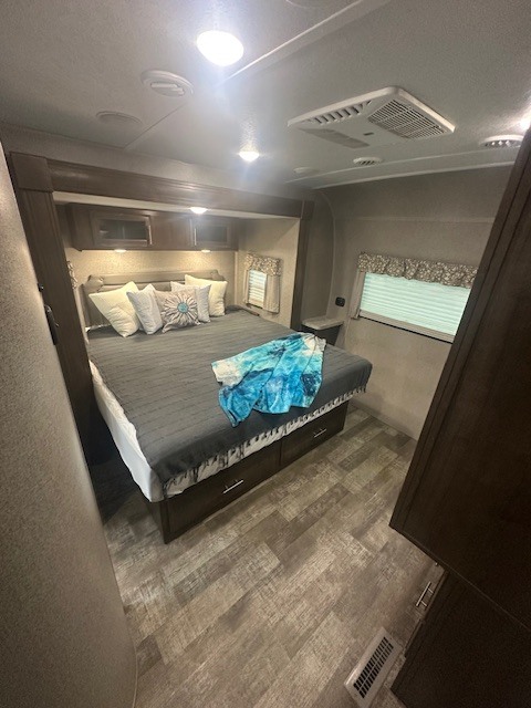 Inside this modern RV rental: a spacious bedroom featuring a large bed with storage, overhead cabinets, and bright windows.. Forest River Rockwood 2019