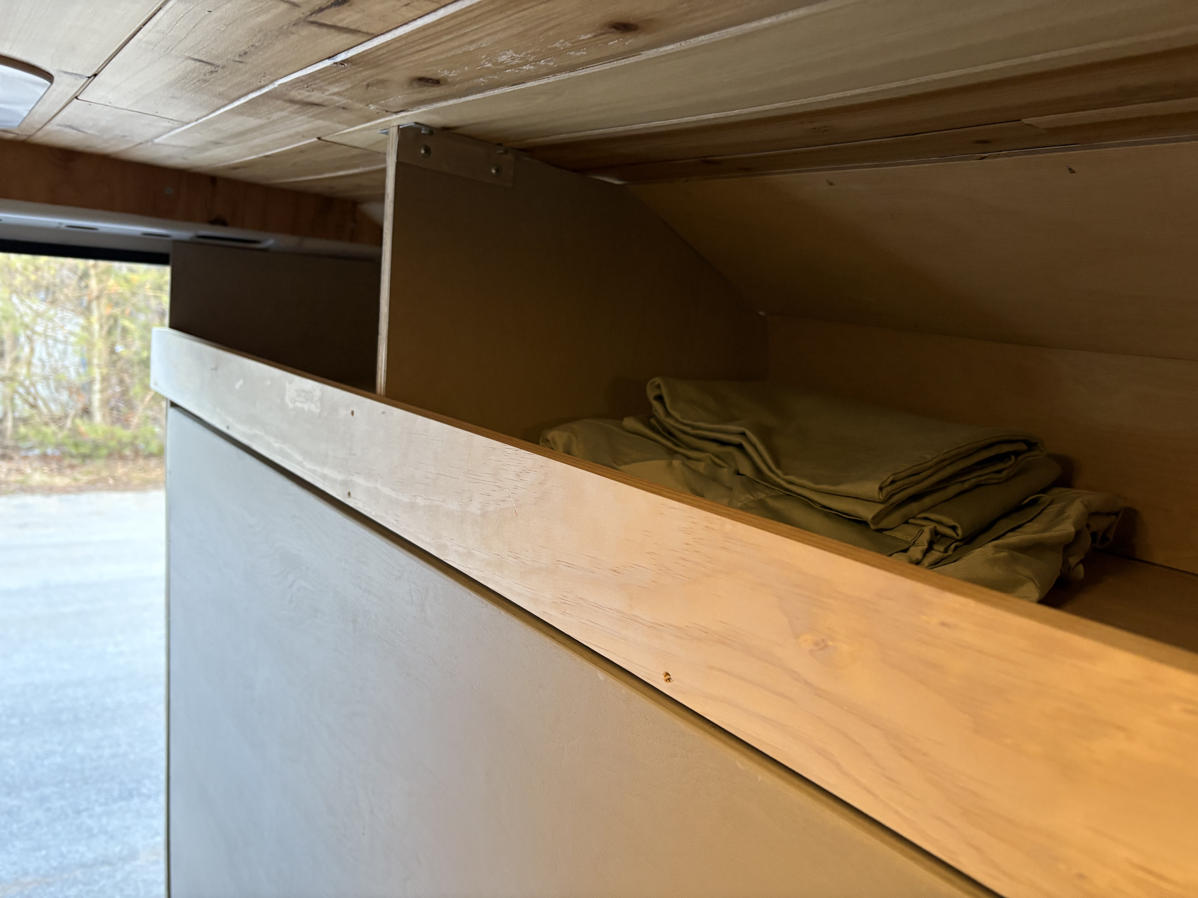 RV rental: Light wood interior featuring a custom shelving unit with neatly folded olive bedding, ideal for camper van storage.. Dodge Sprinter Van 2021