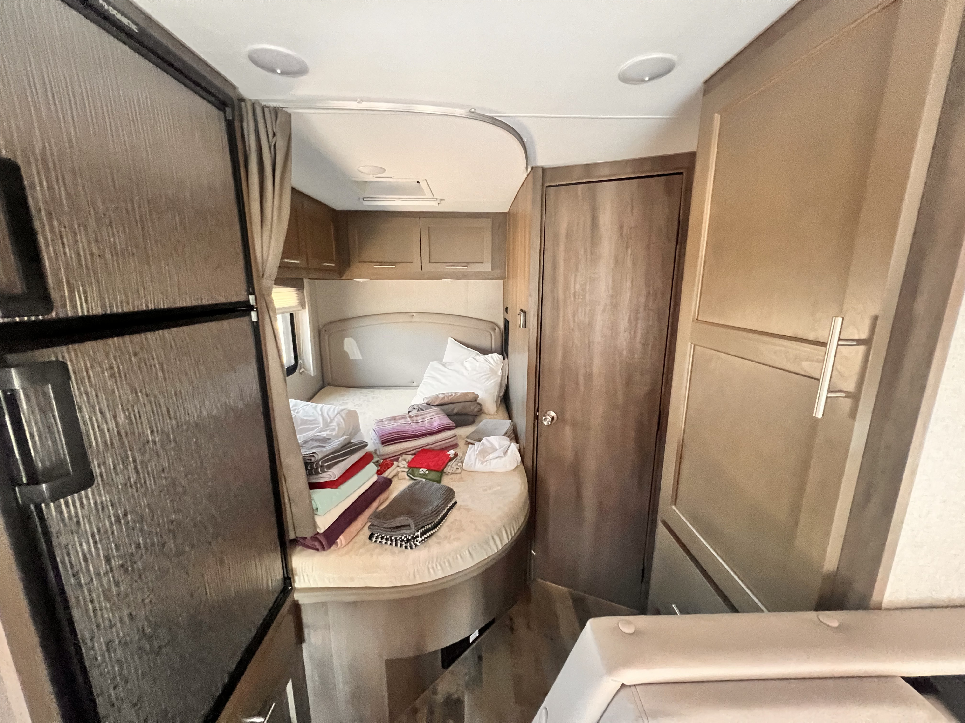 Cozy RV rental bedroom features a bed with linens, overhead cabinets, a refrigerator, and a privacy door.. Adventurer 23RB 2024