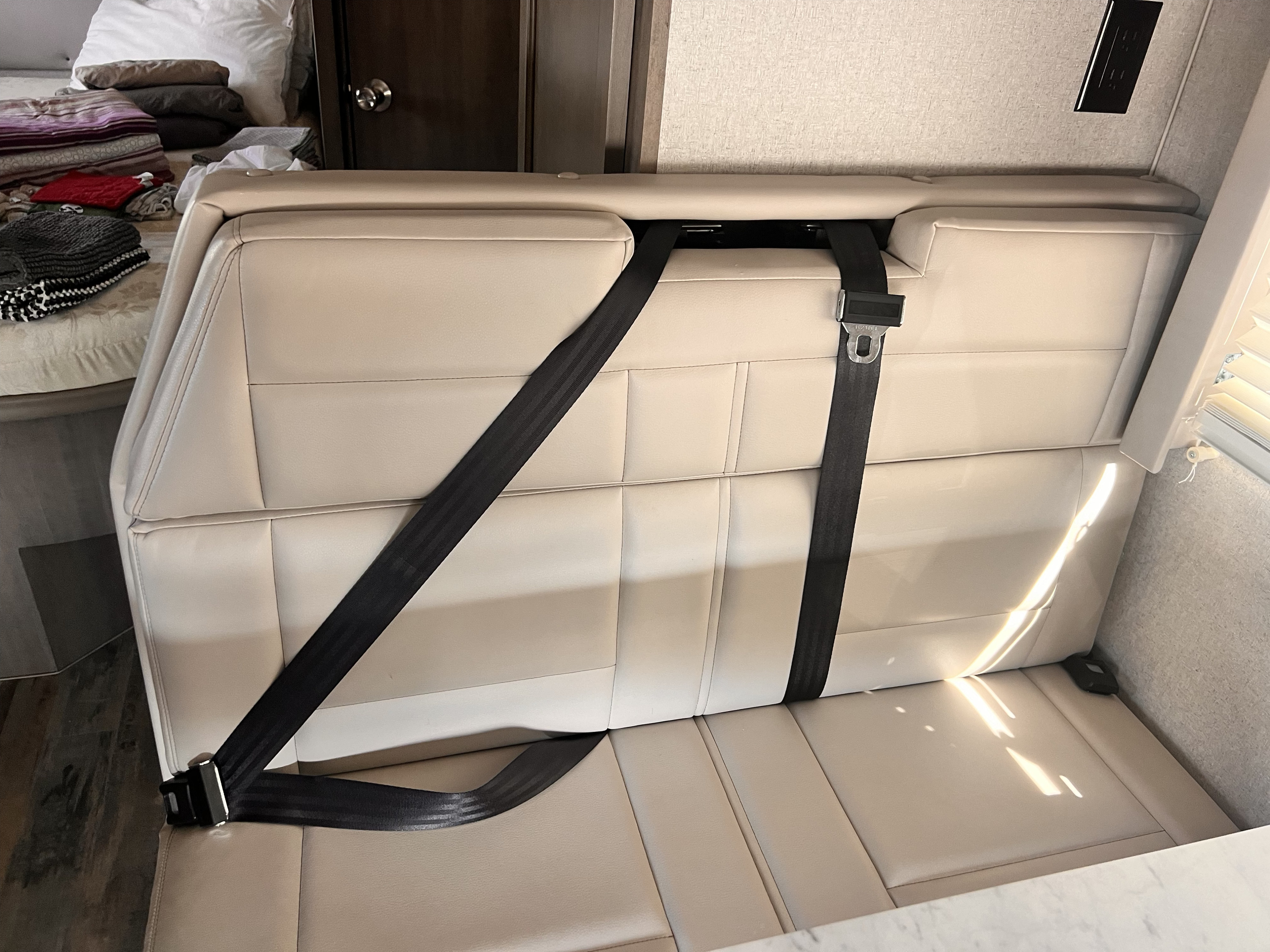 RV rental interior: a clean beige dinette with buckled seatbelts, adjacent to a neatly made bed.. Adventurer 23RB 2024